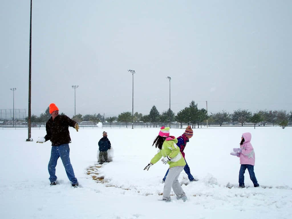 Snowball Fight 桌布 壁紙 — 孩子們和一位成人在多雲的天空下，於廣闊的雪地上開心地丟雪球。