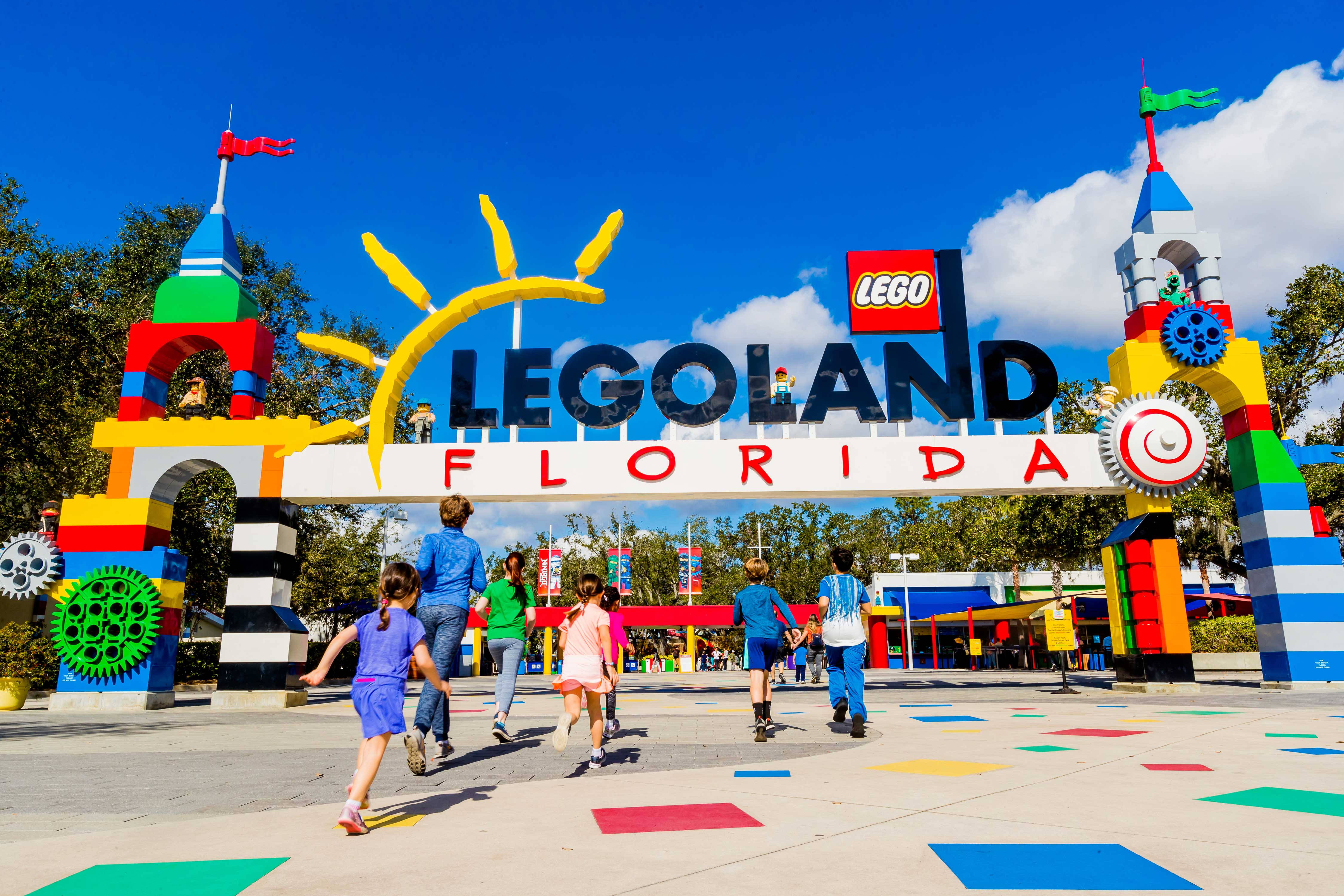 小孩動圖 桌布 壁紙 — 孩子們在明亮的藍天下，快樂地跑向 LEGOLAND Florida 色彩繽紛的 LEGO 主題入口。