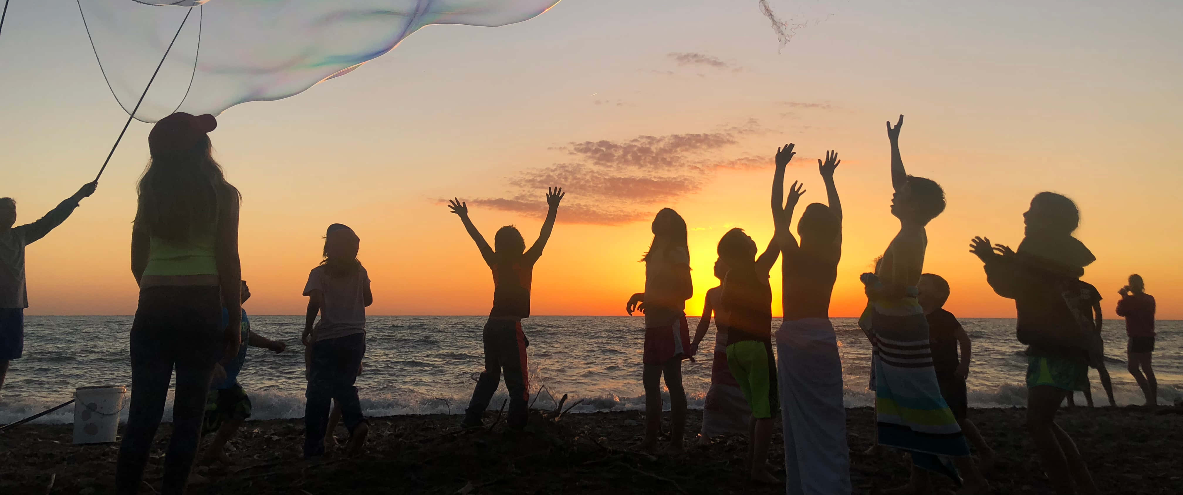 Beach Party 桌布 壁紙 — 孩子們在沙灘上以充滿活力的日落為背景，形成剪影，快樂地追逐並戳破巨大的肥皂泡。