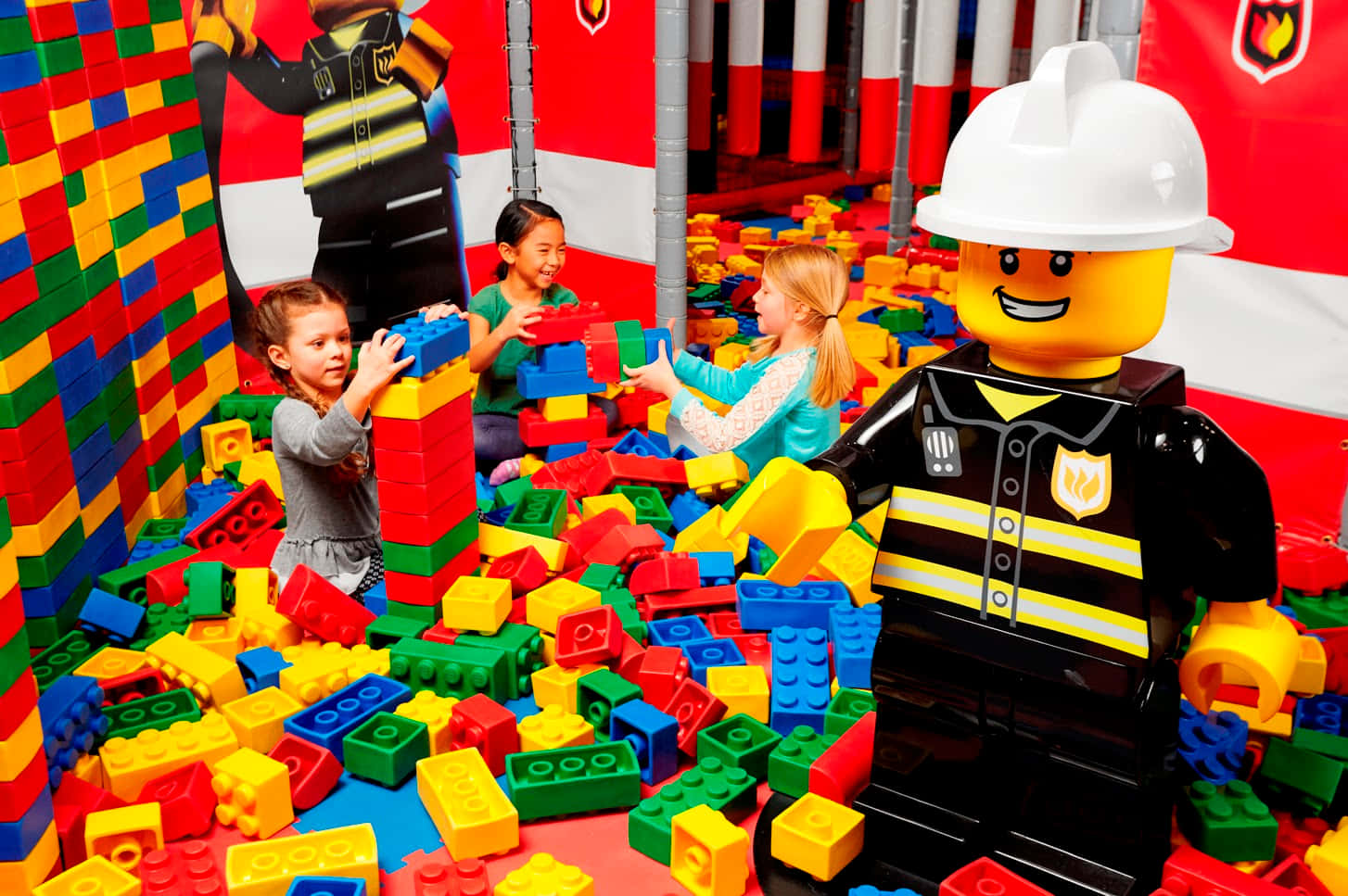 Legoland 桌布 壁紙 — 孩子們在色彩繽紛的LEGO積木中快樂玩耍，附近有一個大型LEGO消防員人偶。