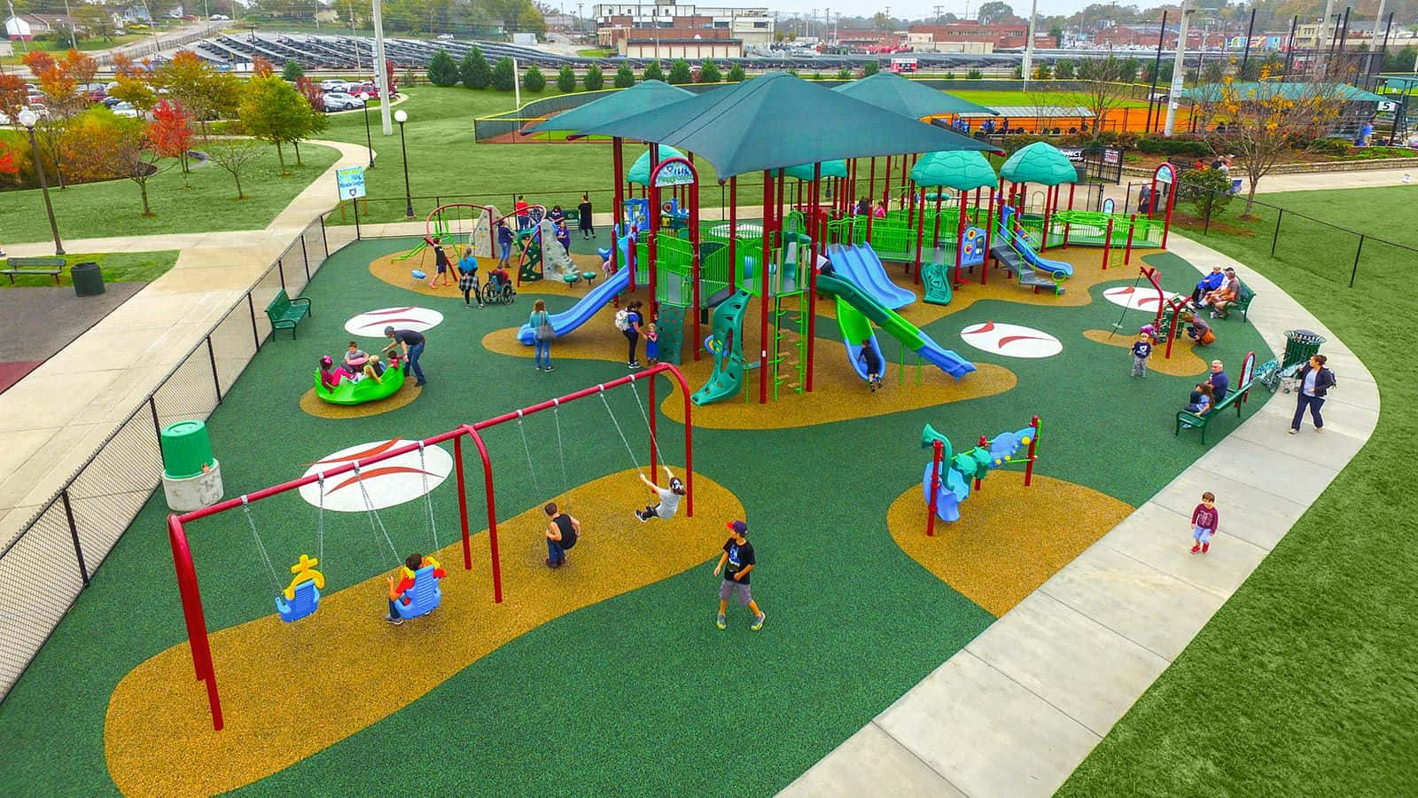 Playground 桌布 壁紙 — 孩子們在色彩繽紛的溜滑梯和鞦韆上玩耍，周圍是秋日樹木環繞的充滿活力的戶外遊樂場。