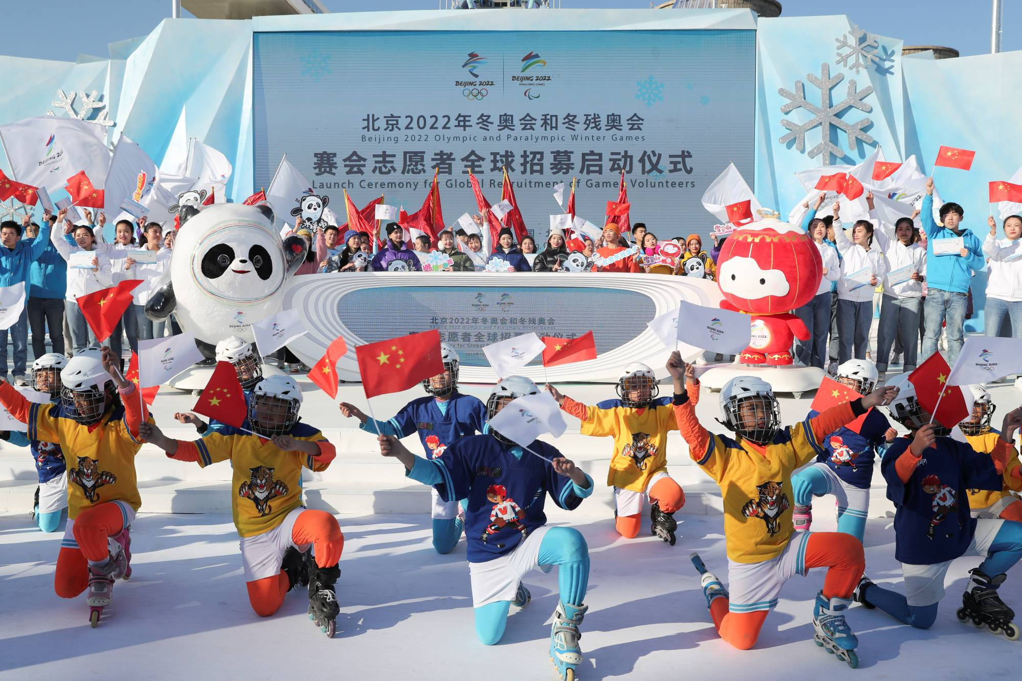 Winter Olympics 桌布 壁紙 — 孩子們穿著色彩繽紛的直排輪和頭盔，在冬季運動會志工活動中揮舞中國國旗，旁邊是奧運吉祥物。