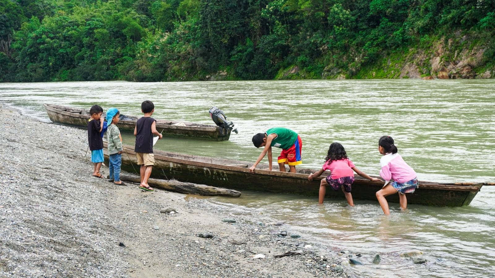 river 桌布 壁紙 — 孩子們頑皮地將木船推入泥濘的河岸，周圍是茂密的綠色森林。