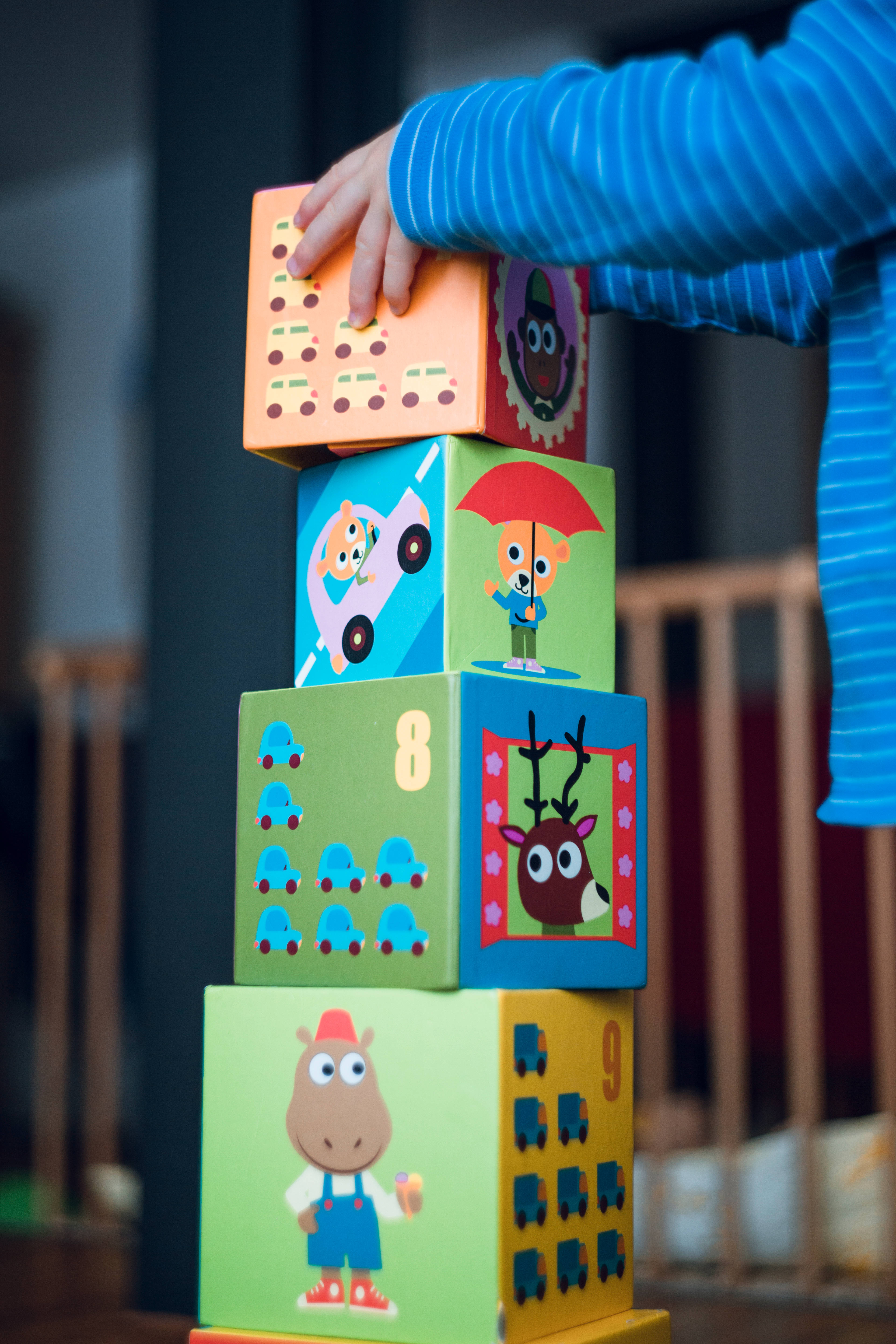 小孩動圖 桌布 壁紙 — 孩子的手在舒適的室內環境中堆疊色彩繽紛的木製積木，上面有卡通動物和車輛。