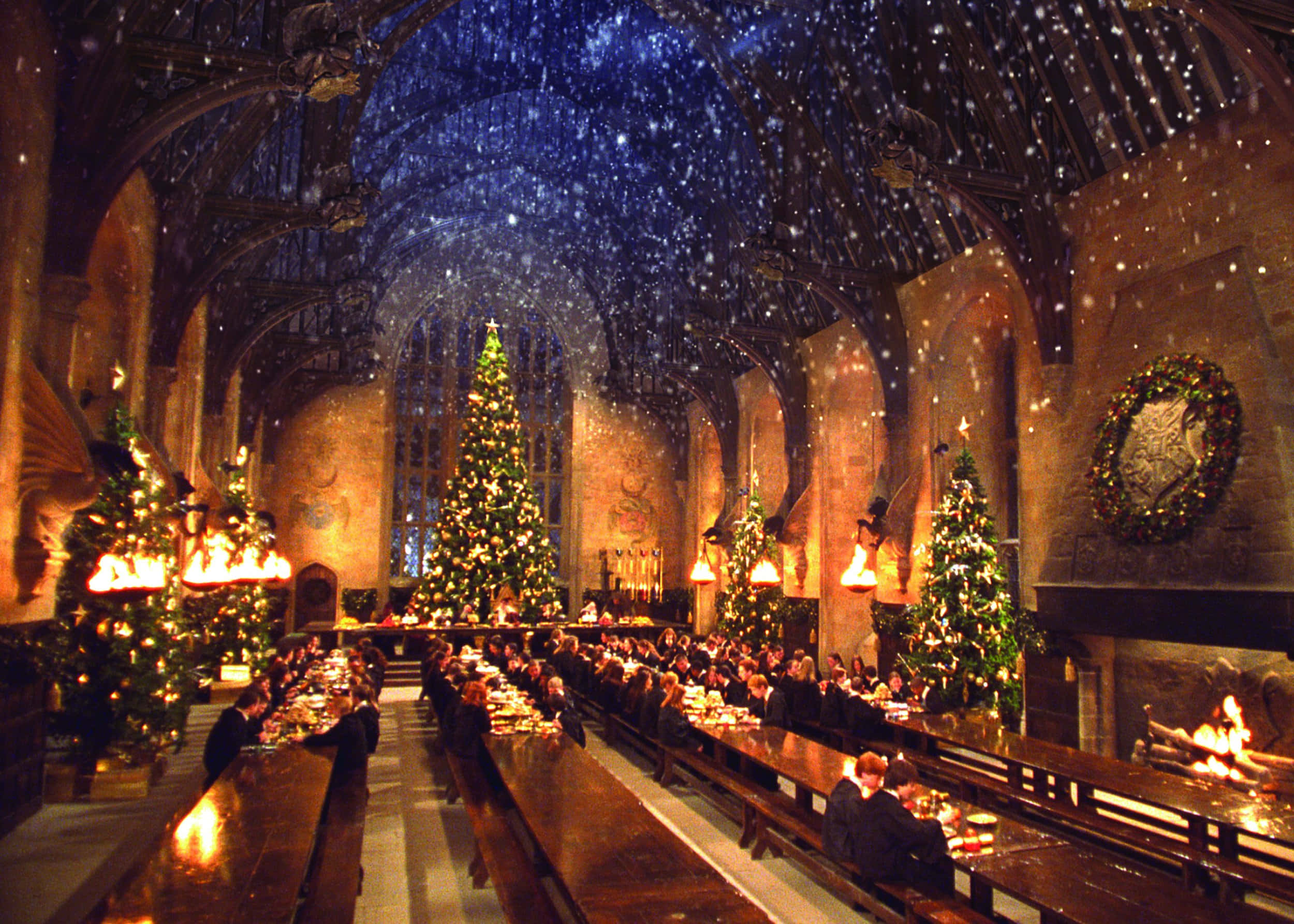 The Hogwarts Great Hall 桌布 壁紙 — 學生們在宏偉的中世紀大廳中，在星光閃爍的魔法天花板下用餐，雪花飄落在高聳的聖誕樹周圍。