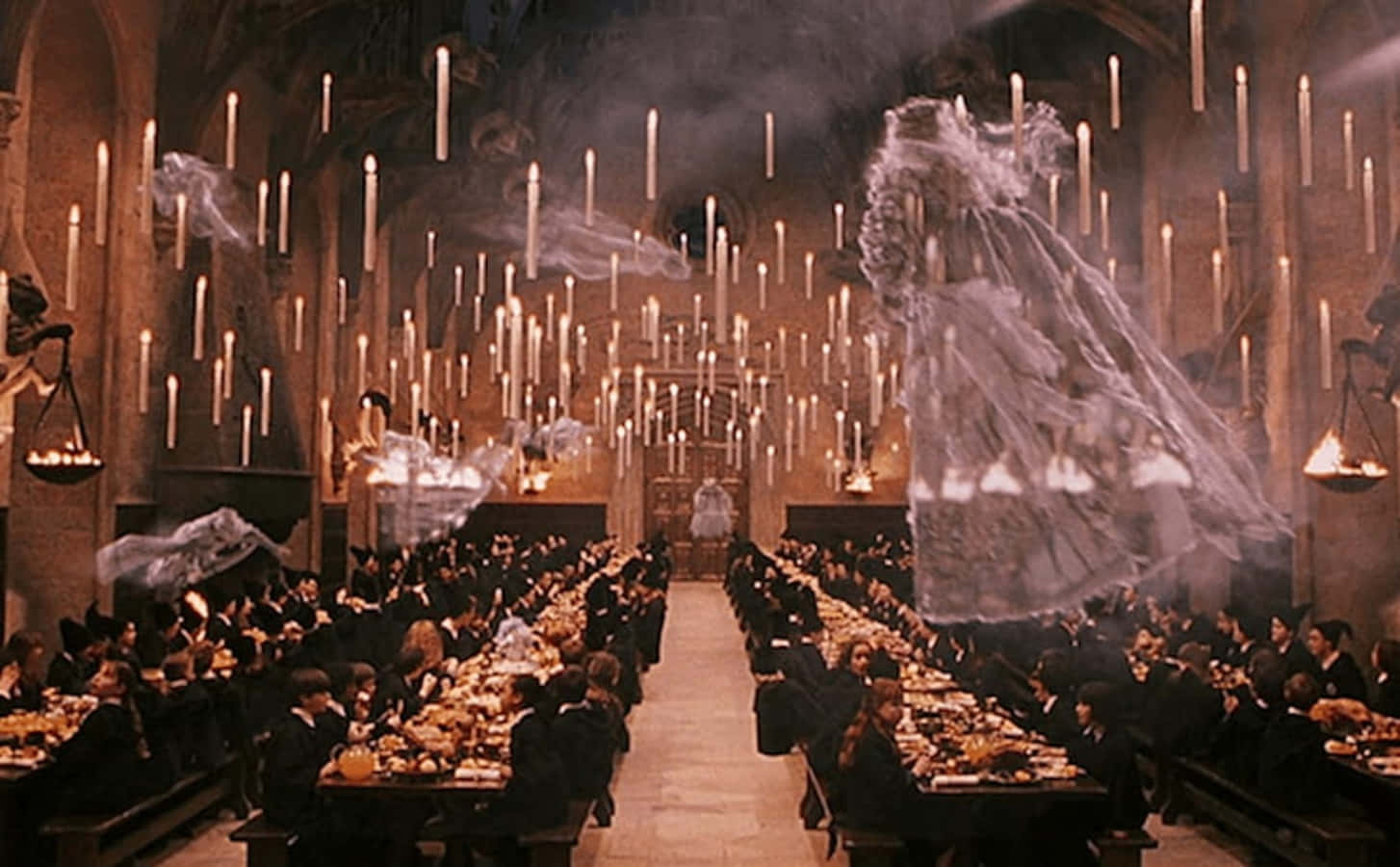 The Hogwarts Ghosts 桌布 壁紙 — 學生們在宏偉的石廳中用餐，鬼魂般的身影在懸掛的蠟燭間漂浮，散發出溫暖的光芒。
