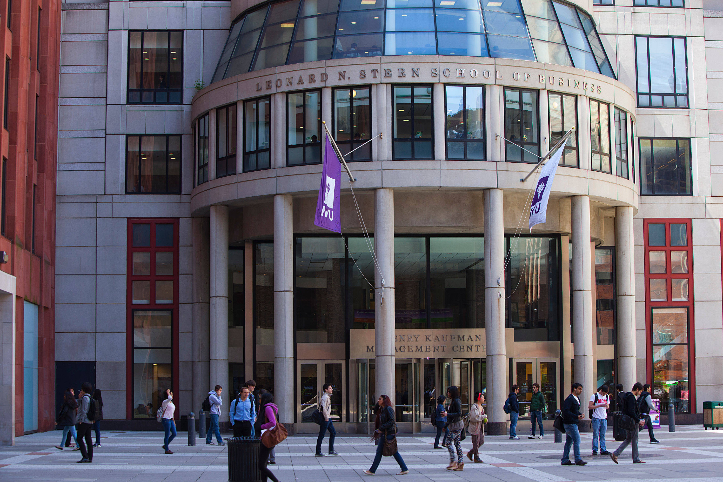 建築 桌布 壁紙 — 學生和教職員走過現代玻璃和石材建造的 Leonard N. Steen School of Business 大樓前的廣場。