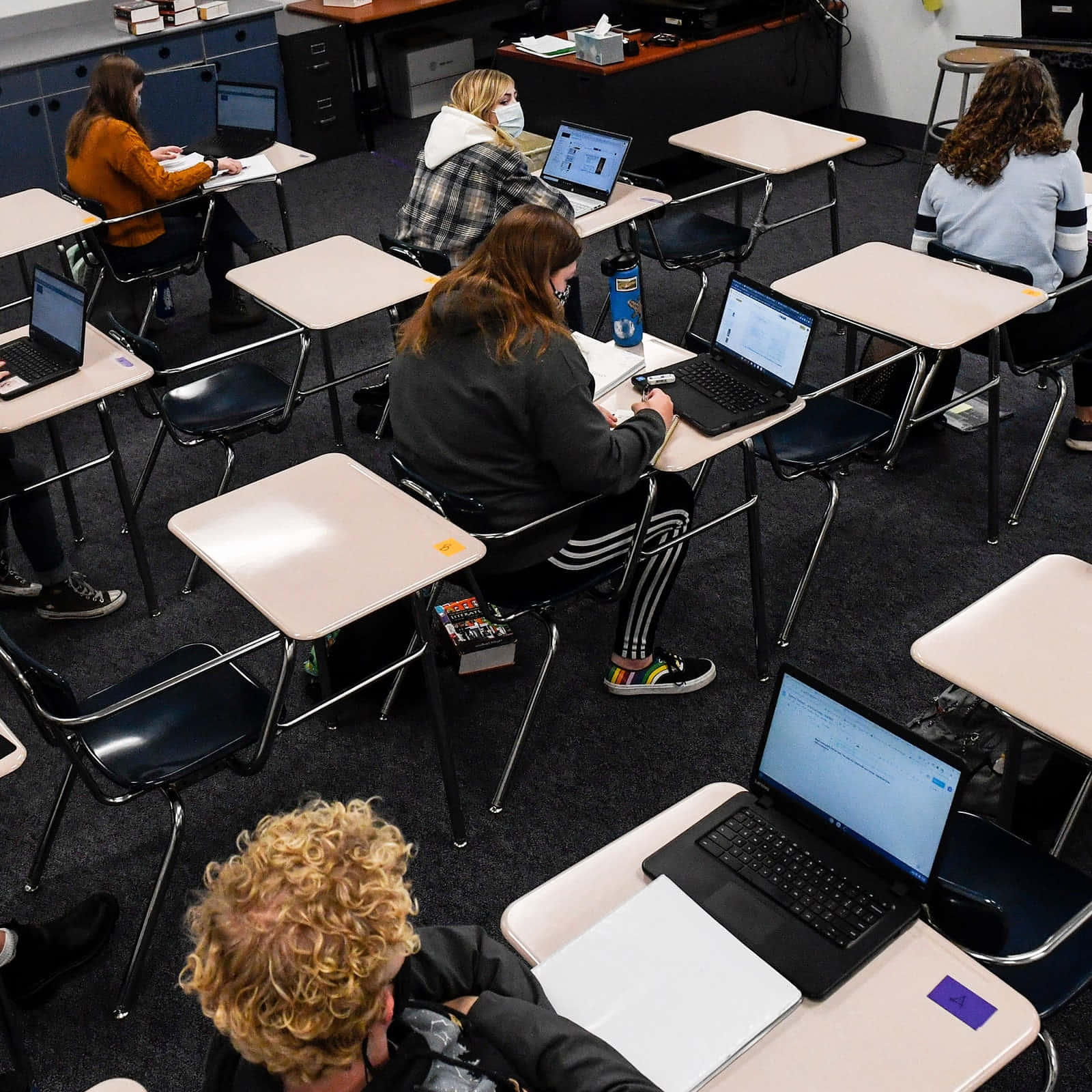Classroom 桌布 壁紙 — 學生在教室裡坐在書桌前使用筆記型電腦，並在遠距學習期間佩戴口罩。
