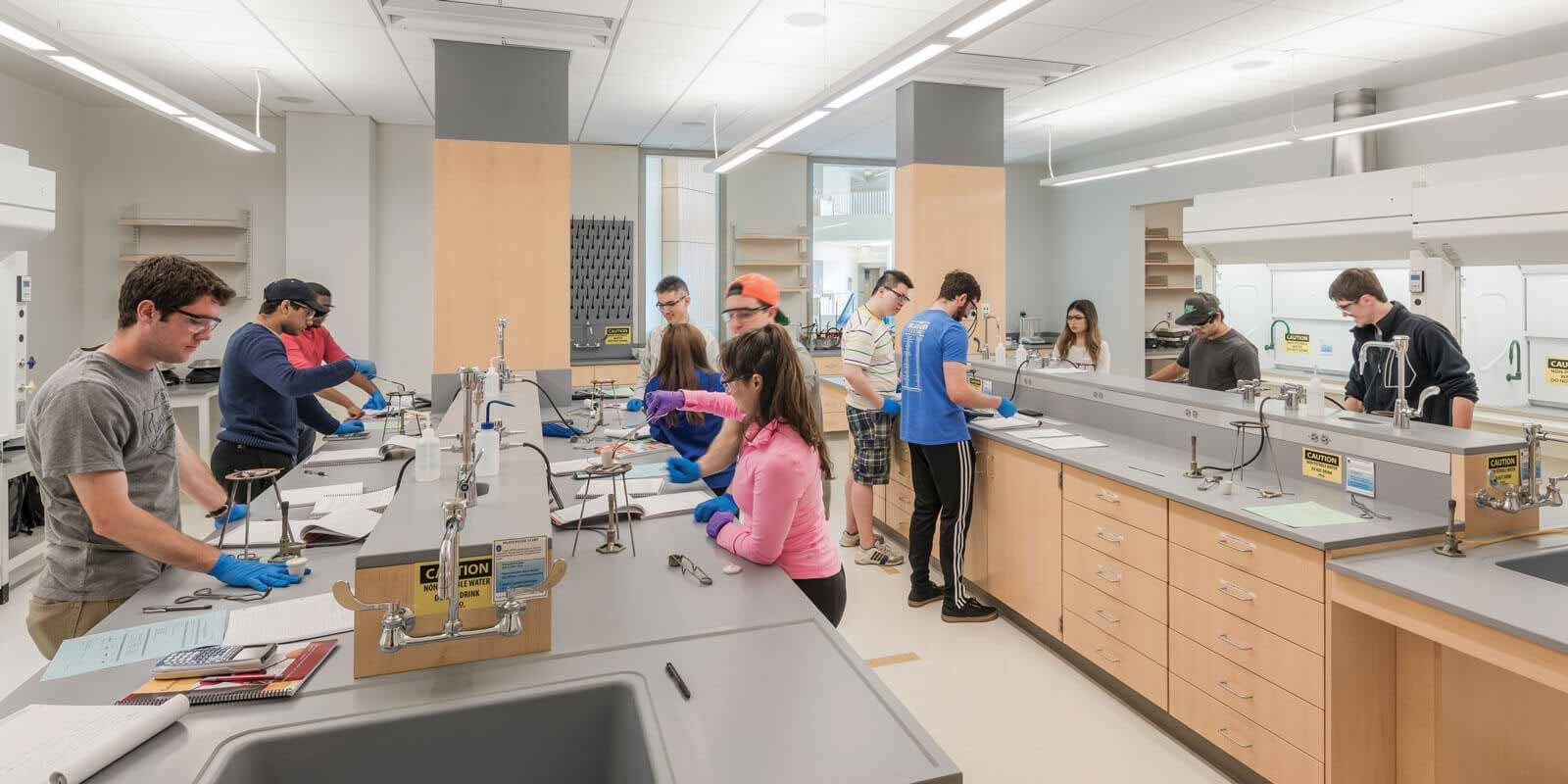 student 桌布 壁紙 — 學生在現代科學實驗室戴著手套和護目鏡，在有水槽和設備的長檯上工作。