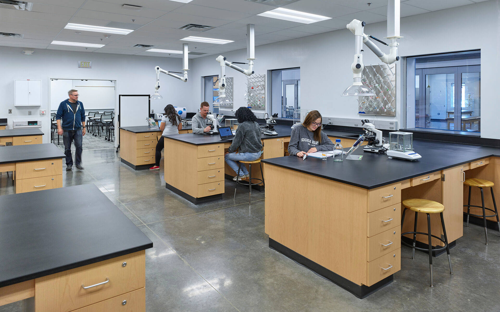Laboratory 桌布 壁紙 — 學生在現代科學教室的實驗站工作，上方有通風櫥和明亮的螢光燈。