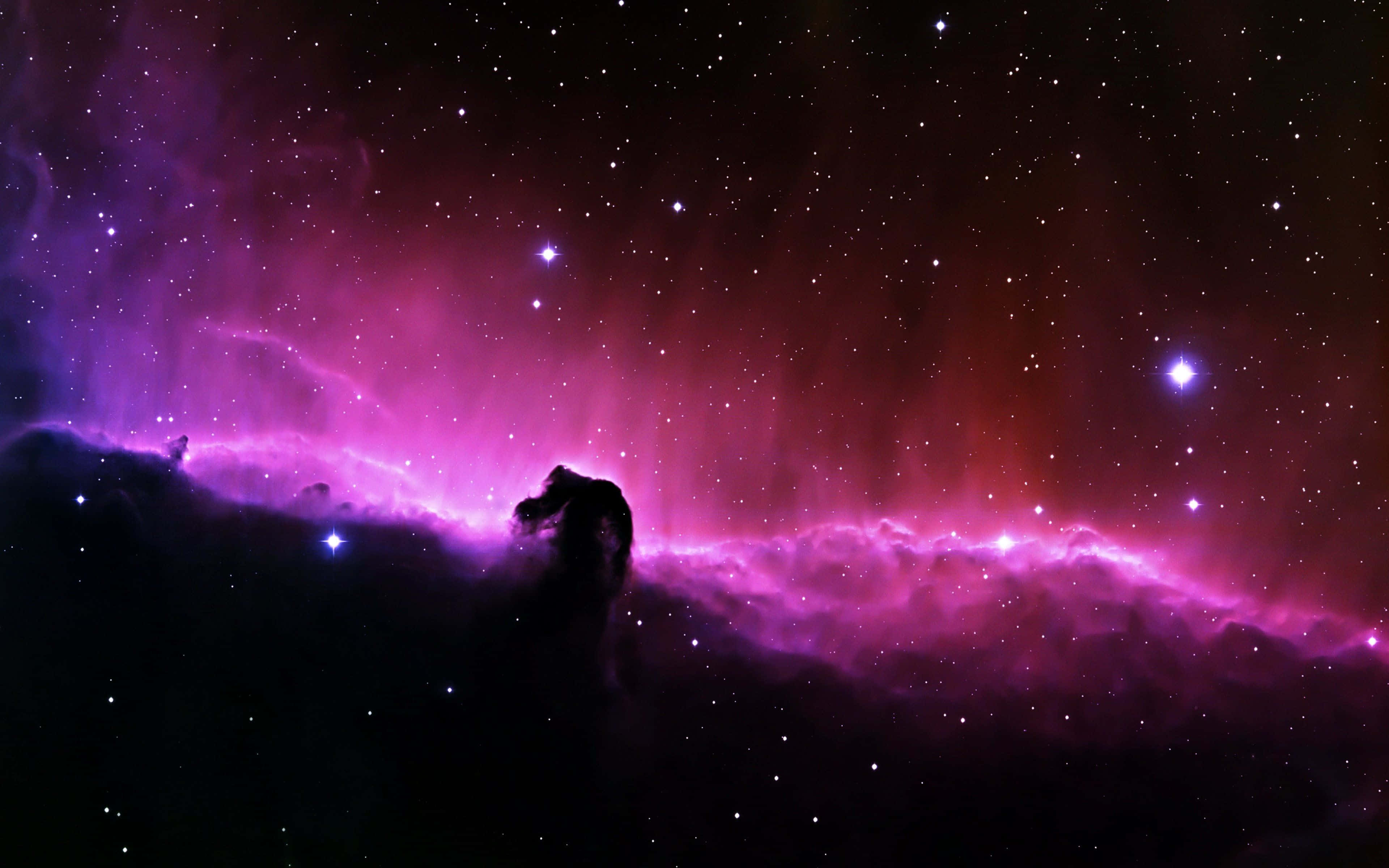 粉紅銀河 桌布 壁紙 — 宇宙星雲在星空背景下散發出充滿活力的紫色和紅色色調，並帶有天體形成的黑色剪影。
