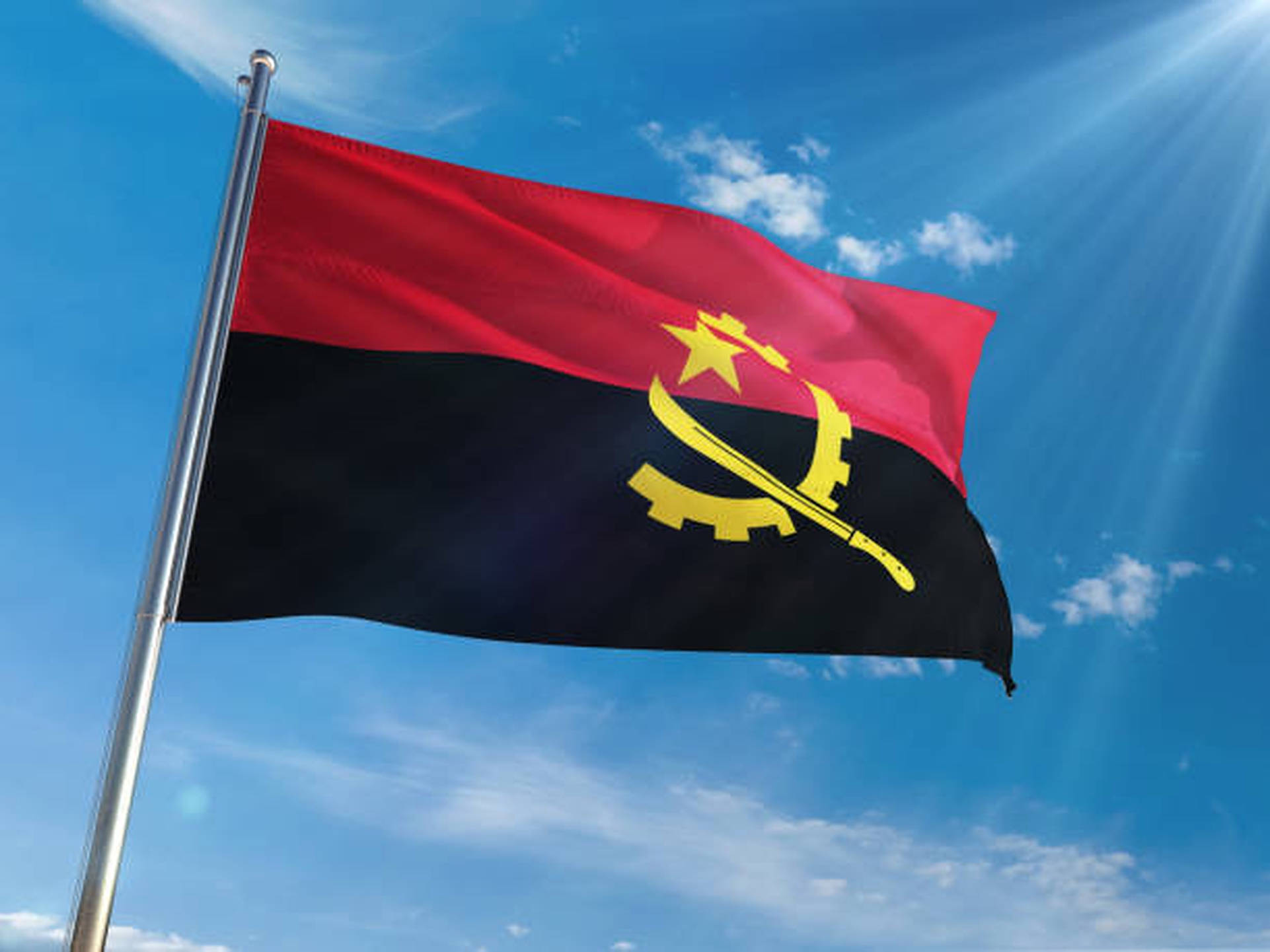 Angola 桌布 壁紙 — 安哥拉國旗在明亮的藍天下驕傲地飄揚，陽光穿過散落的雲層。