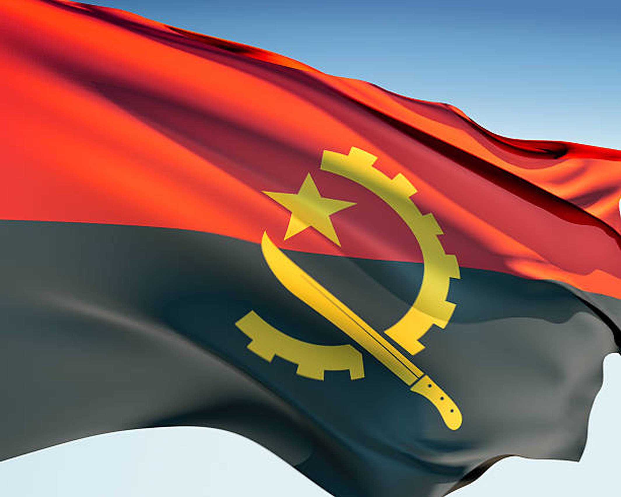 Angola 桌布 壁紙 — 安哥拉國旗在清澈的藍天下動態飄揚，帶有醒目的紅黑條紋和金色徽章。
