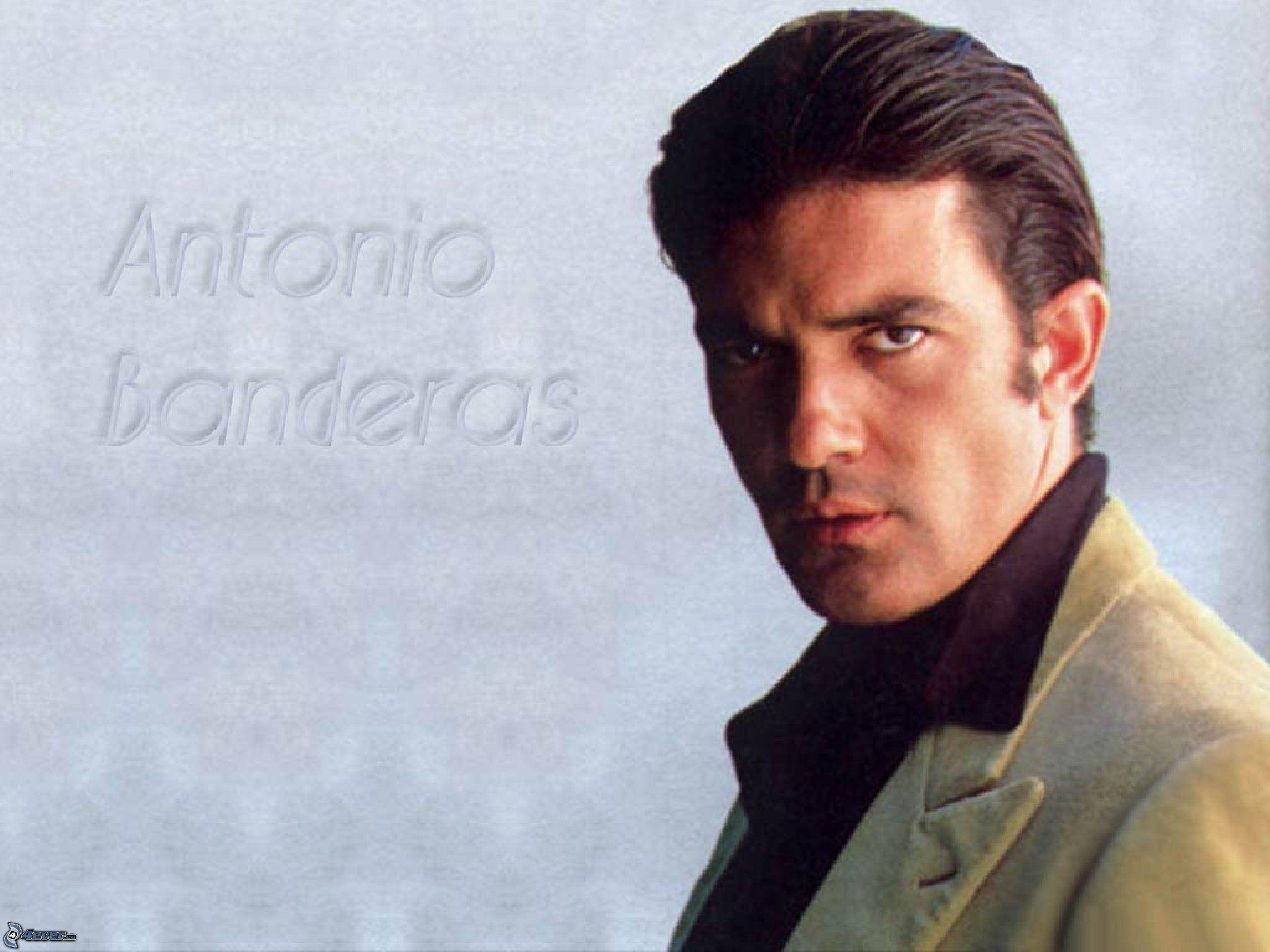 antonio banderas 桌布 壁紙 — 安東尼奧·班德拉斯穿著輕便外套，在柔和的灰色背景前凝視，他的名字微妙地刻在背景中。