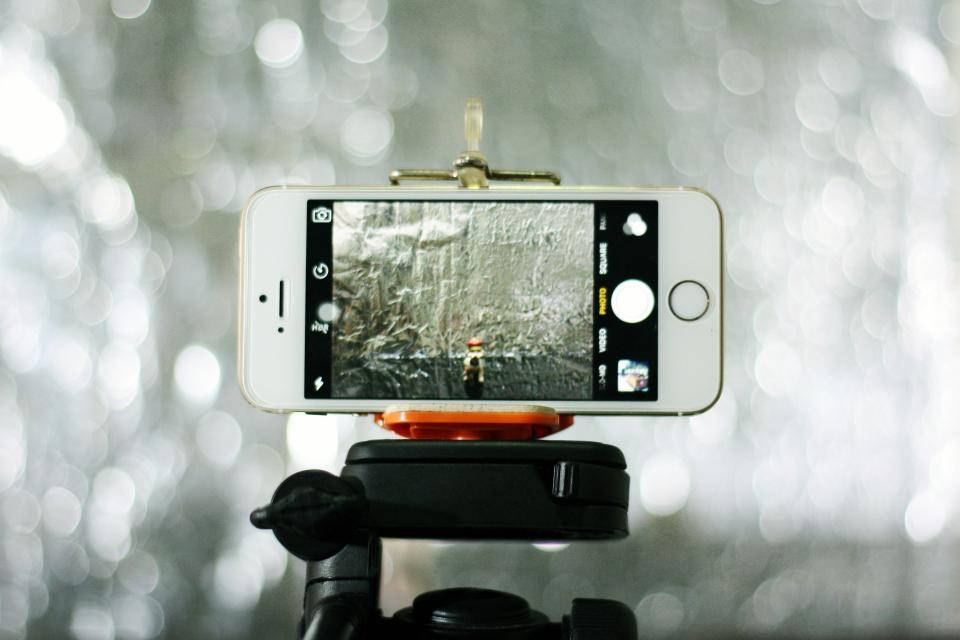 photography iPhone 桌布 壁紙 — 安裝在三腳架上的智慧型手機捕捉到一個孤獨的身影在雪地森林中行走，背景帶有散景光效。