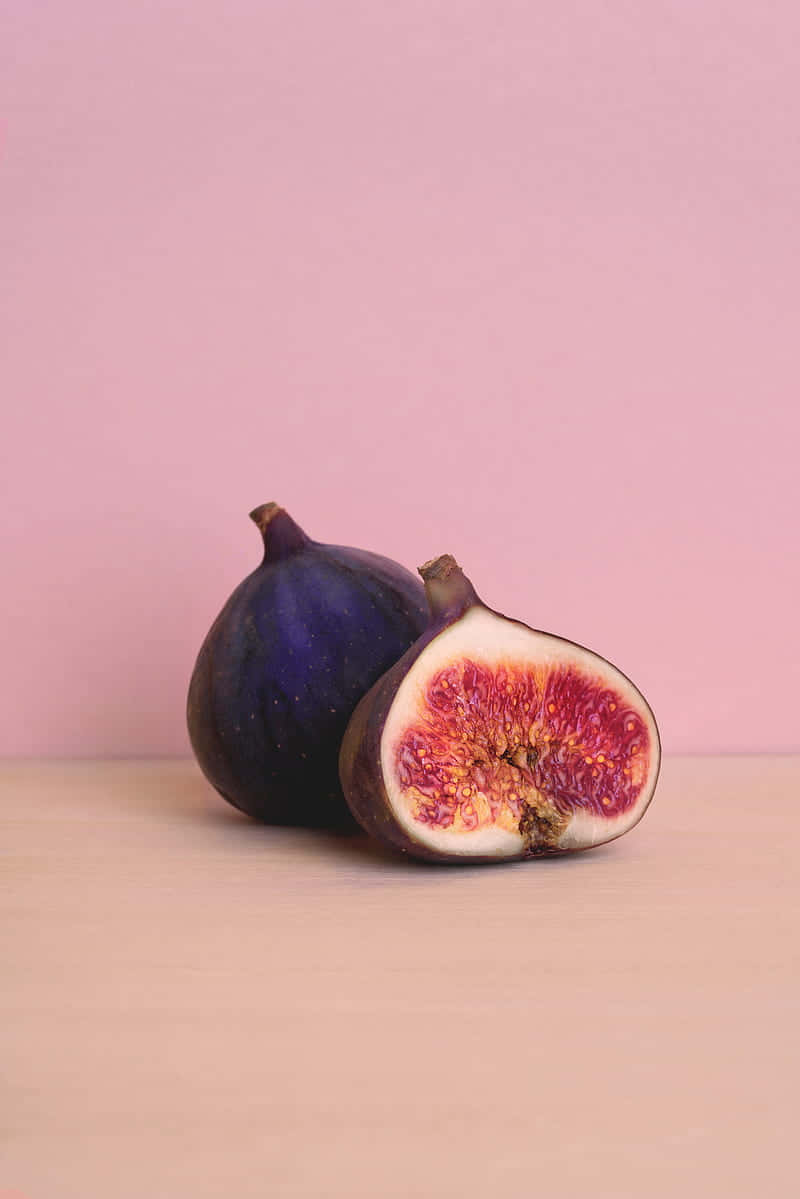 Purple Figs 桌布 壁紙 — 完整和切半的成熟無花果放在木質表面上，背景是柔和的粉紅色。