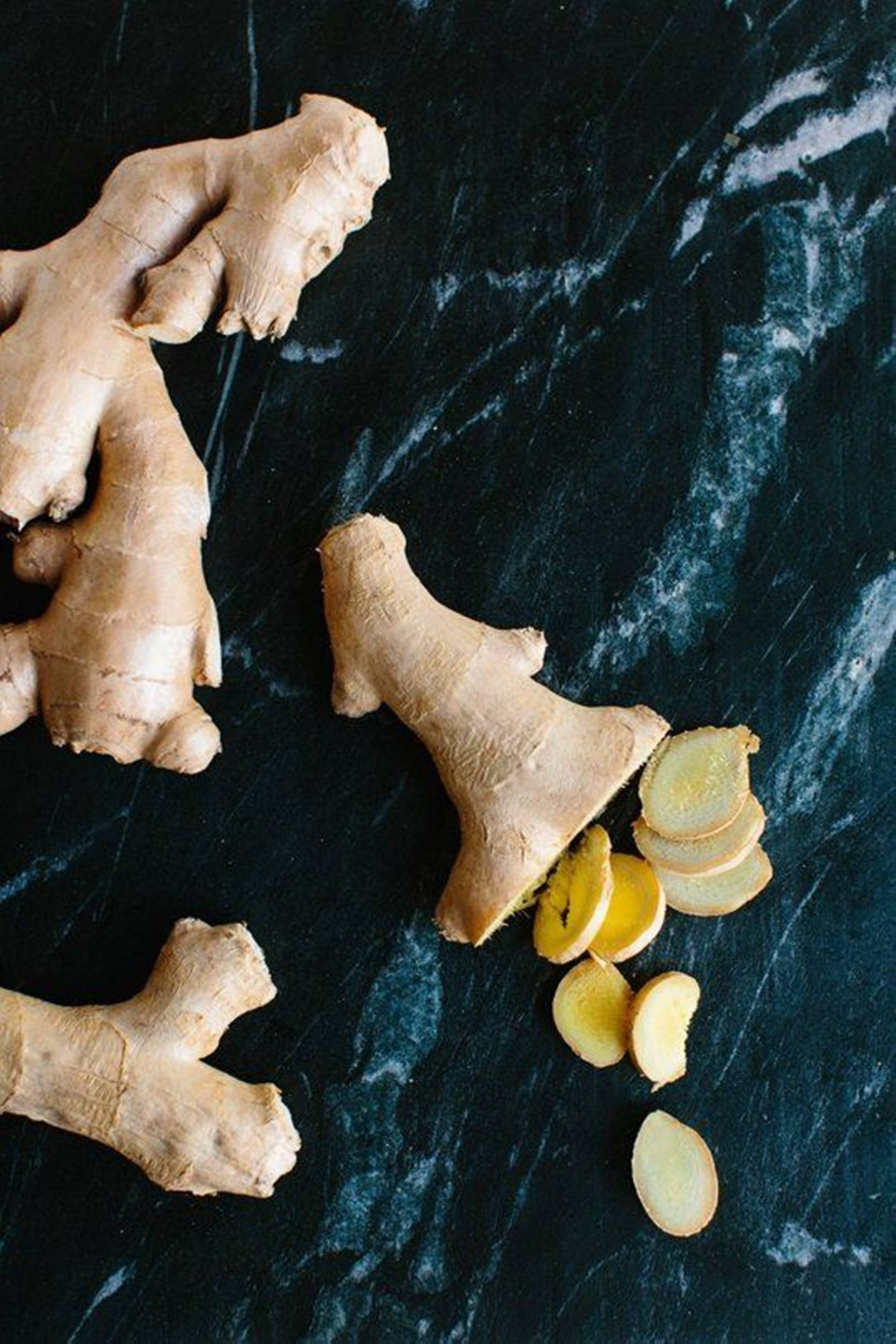 Ginger 桌布 壁紙 — 完整和切片的生薑根放在深色大理石表面上，帶有自然紋理和大地色調。