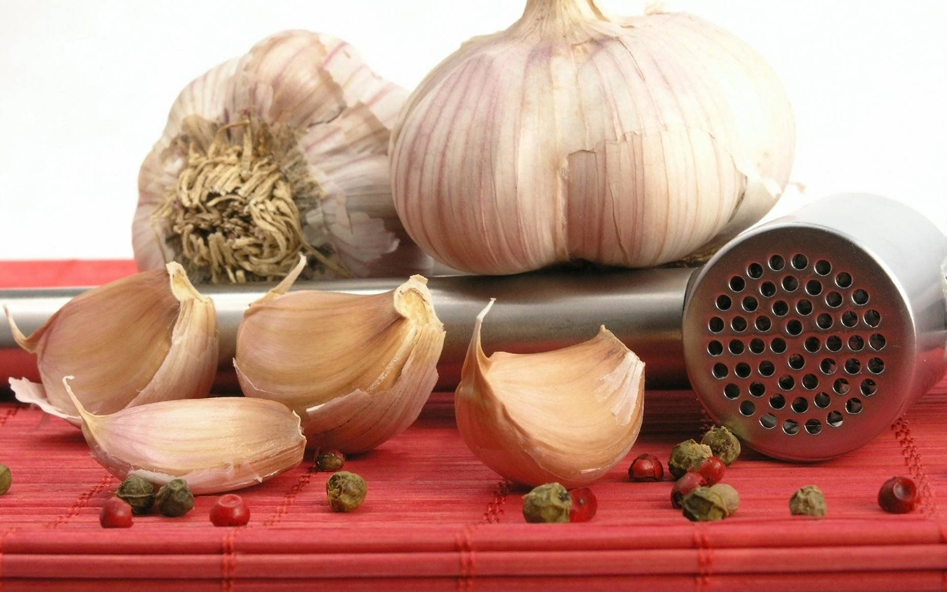 Garlic 桌布 壁紙 — 完整和去皮的蒜瓣連同胡椒粒放在紅色竹蓆上，旁邊有一個壓蒜器。