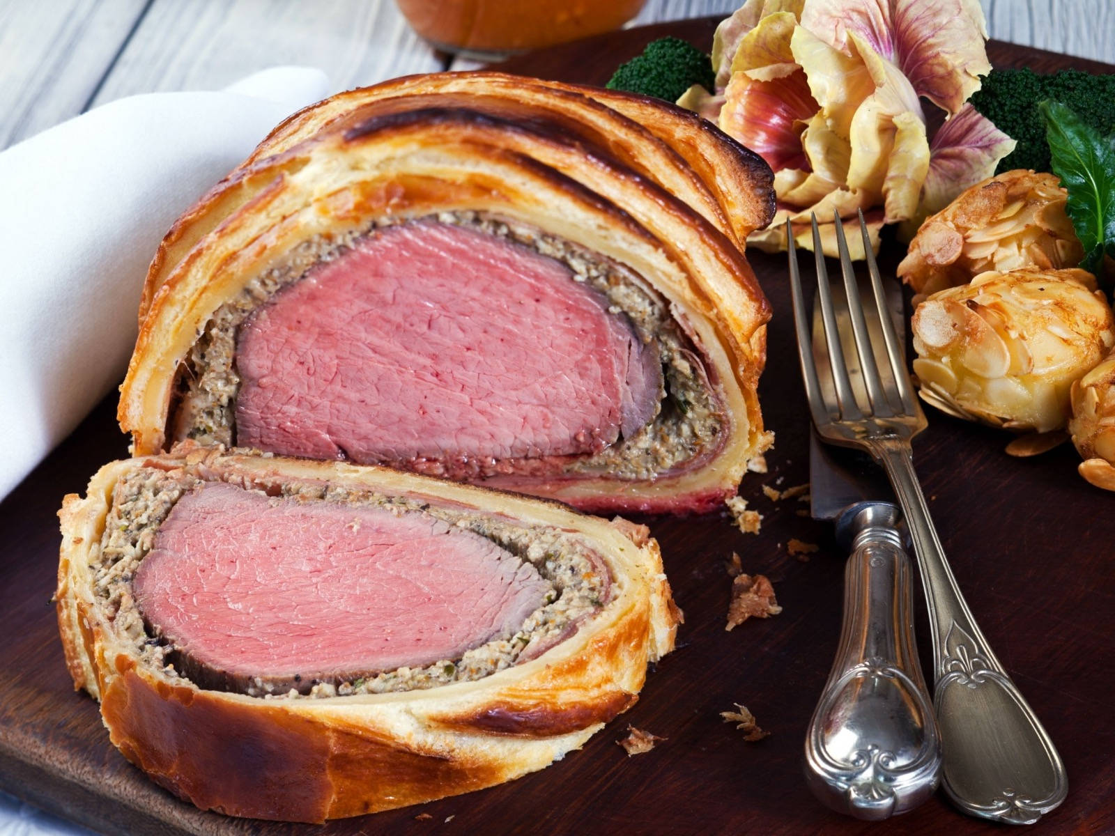 meat 桌布 壁紙 — 完美切片的威靈頓牛排，金黃外皮和粉紅色中心，放在木板上，旁邊有烤蔬菜和華麗的銀器。