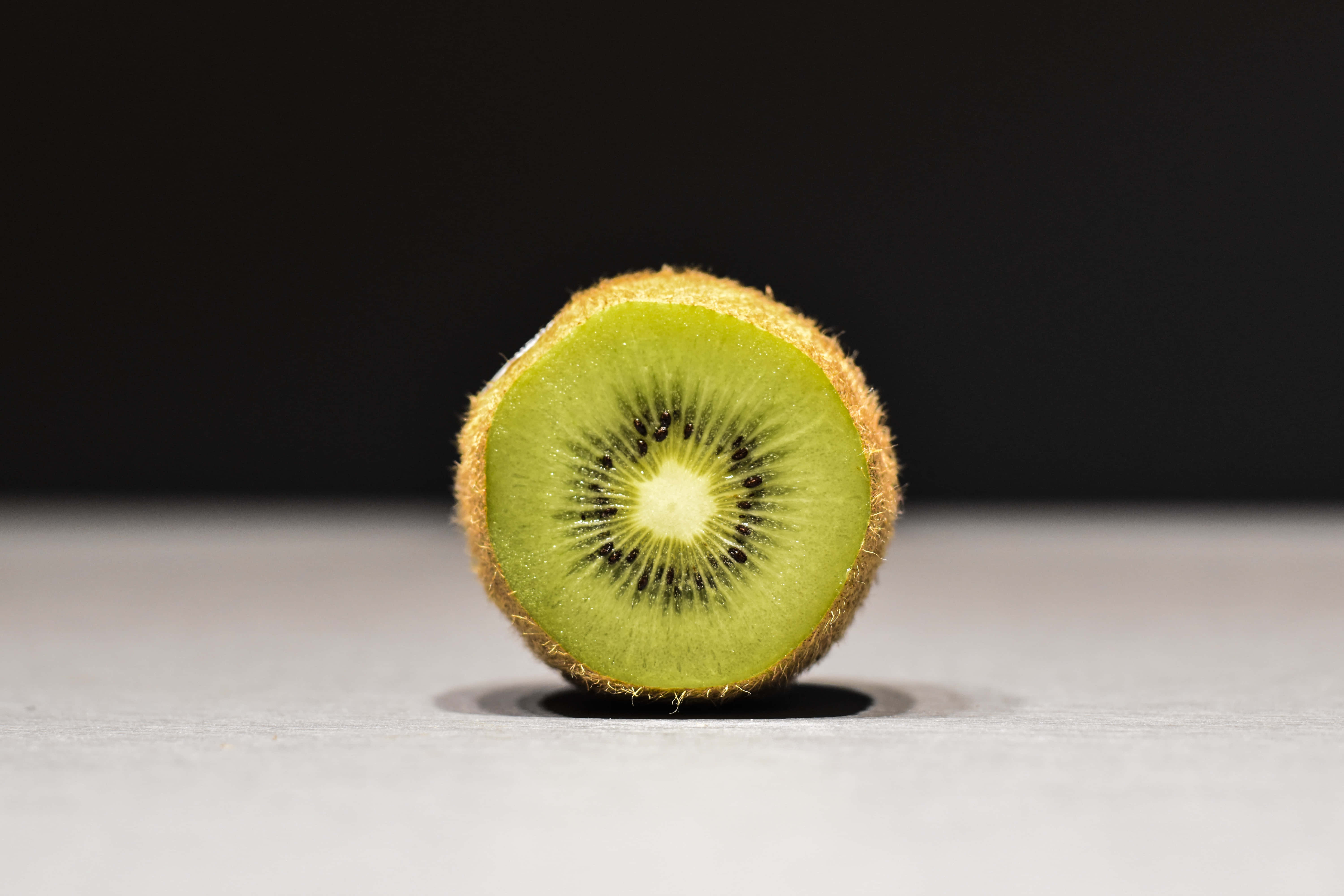 Kiwi 桌布 壁紙 — 完美切開的奇異果在鮮明的深色背景下展現出充滿活力的綠色果肉和黑色種子。