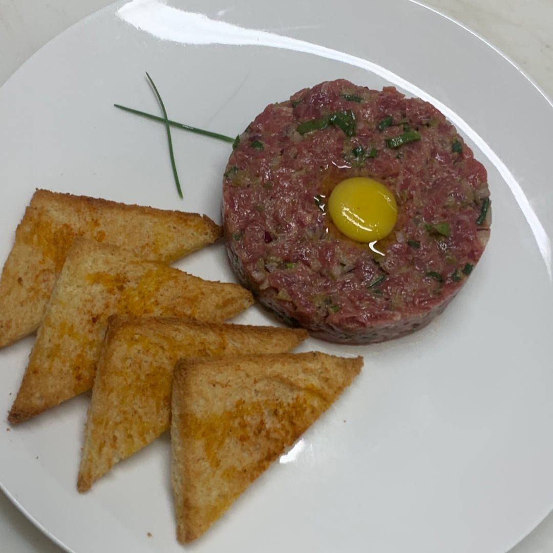 meat 桌布 壁紙 — 完美圓形的生牛肉他他，上面放有生蛋黃，並以細香蔥裝飾，放在白色盤子上，搭配金色三角形吐司。