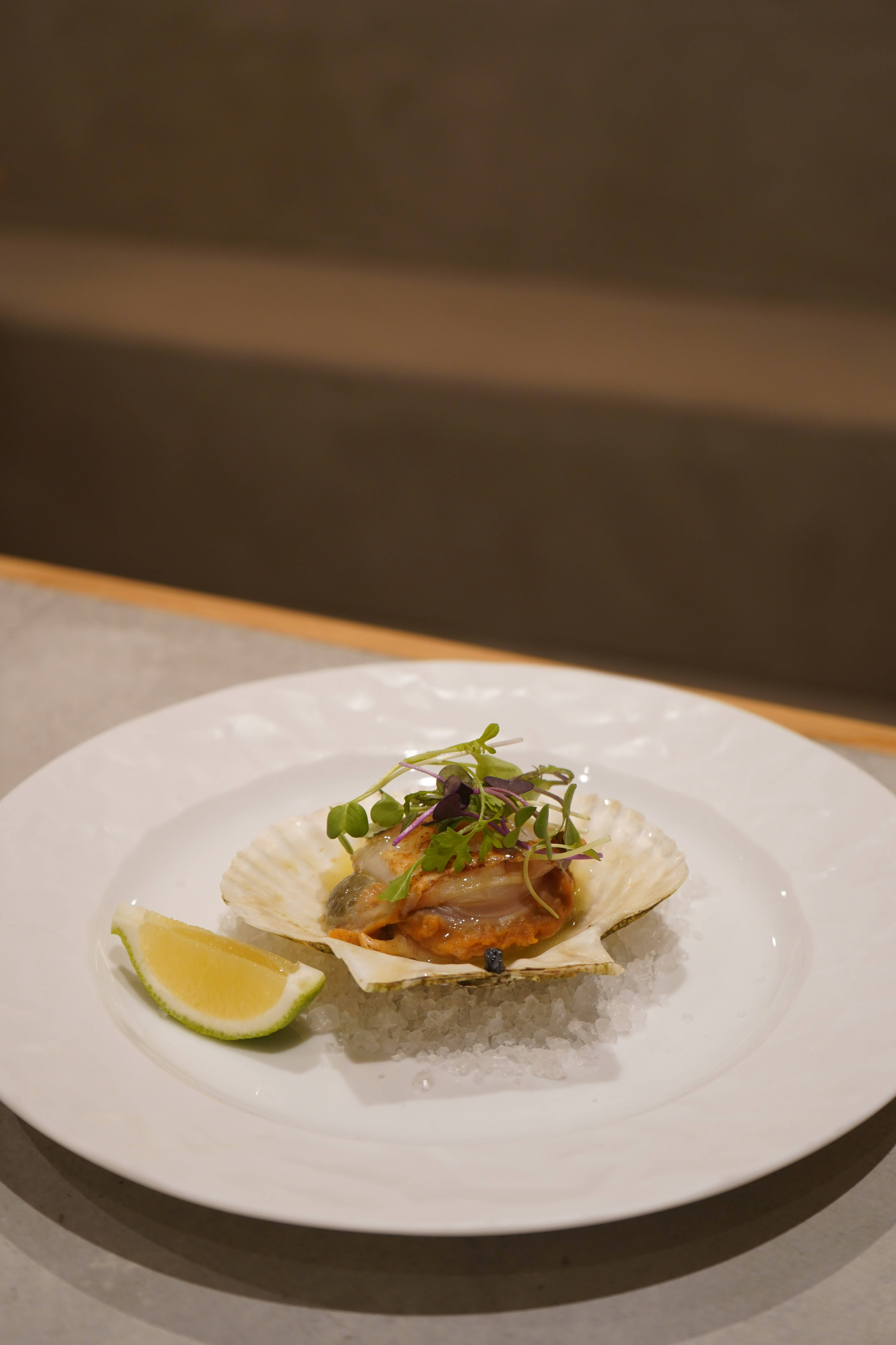 Delicious Food 桌布 壁紙 — 完美擺盤的扇貝在殼中，置於鹽上，配以微型蔬菜和青檸角，放在白色盤子上。