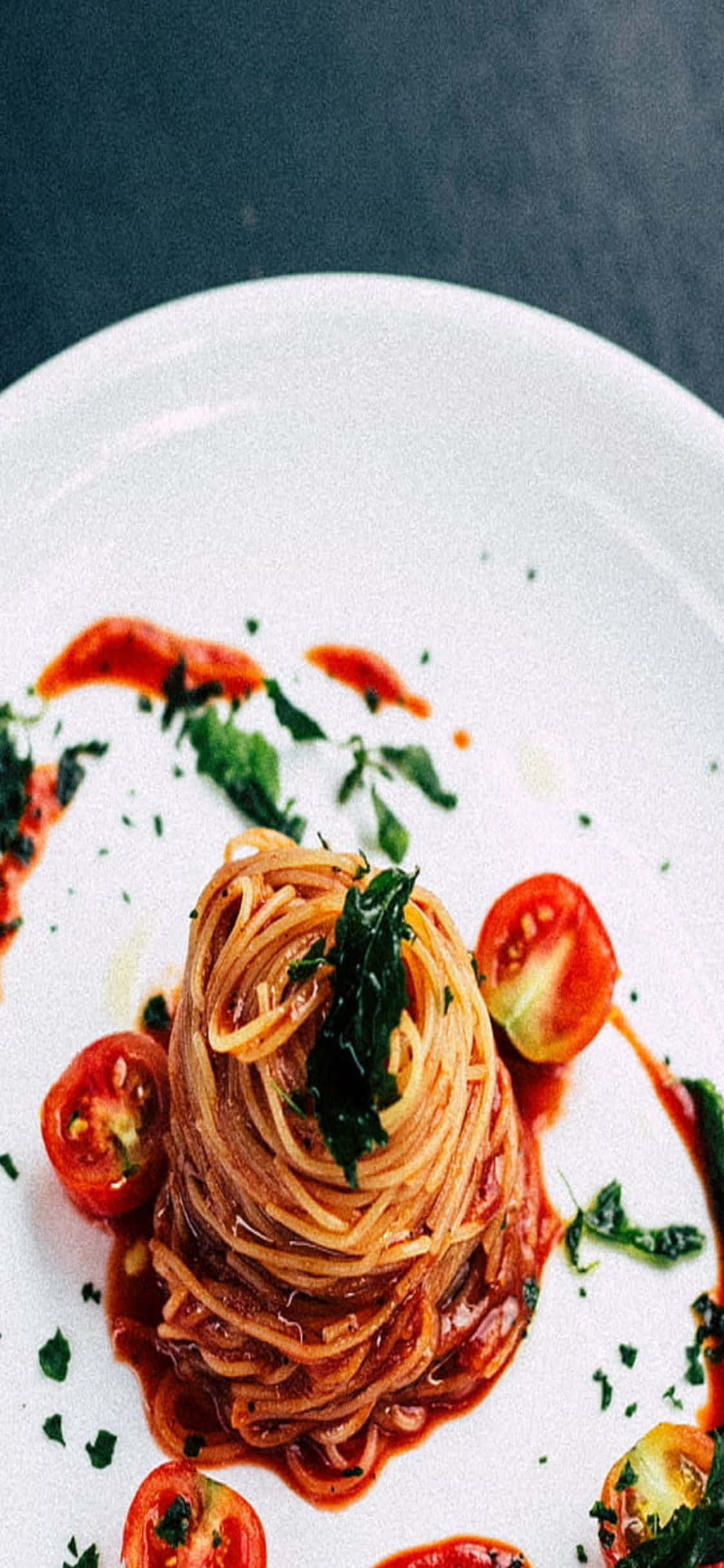 iPhone X Pasta 桌布 壁紙 — 完美擺盤的義大利麵，配上番茄醬、羅勒和對半切開的櫻桃番茄，放在白色盤子上。