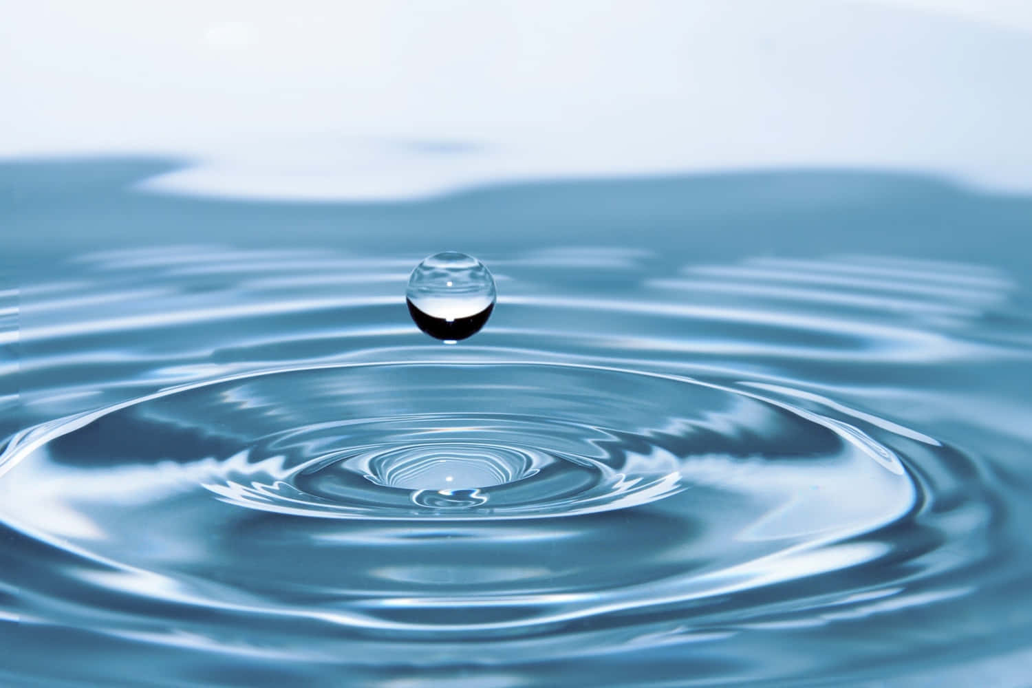 Water Drop 桌布 壁紙 — 完美水滴懸浮在平靜的藍色水面上，以慢動作產生同心漣漪。