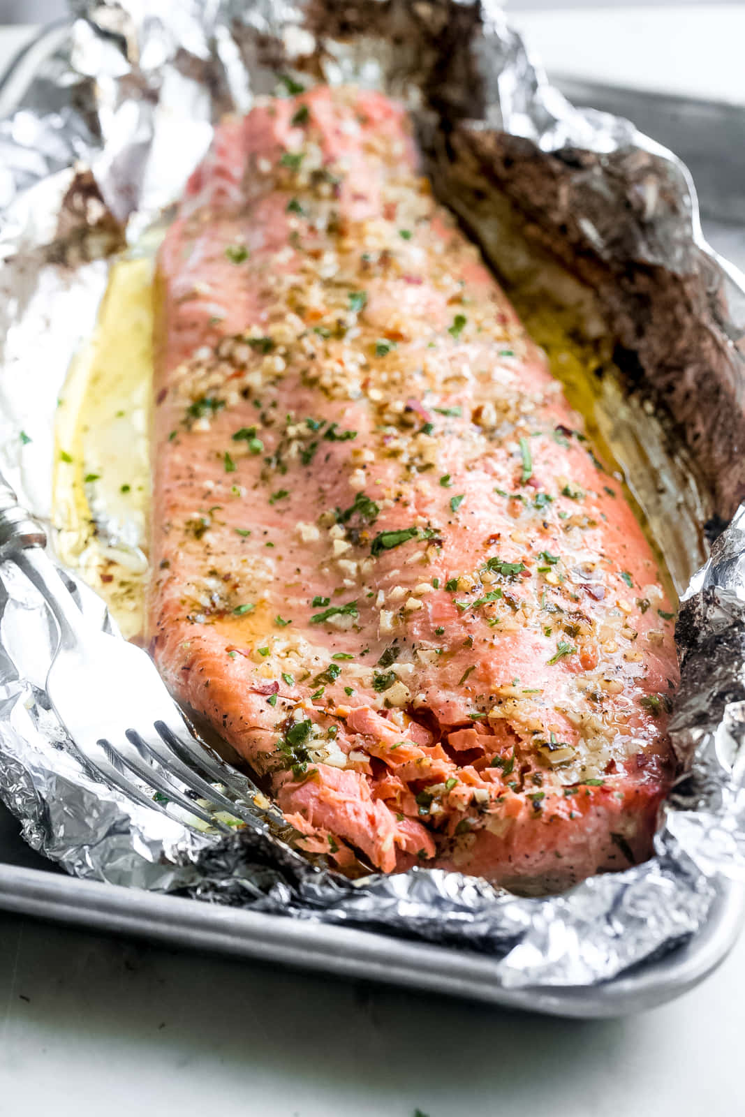 Salmon 桌布 壁紙 — 完美烹調的鮭魚菲力，以香草和大蒜調味，放在錫箔紙上，置於烤盤中，旁邊放著叉子。