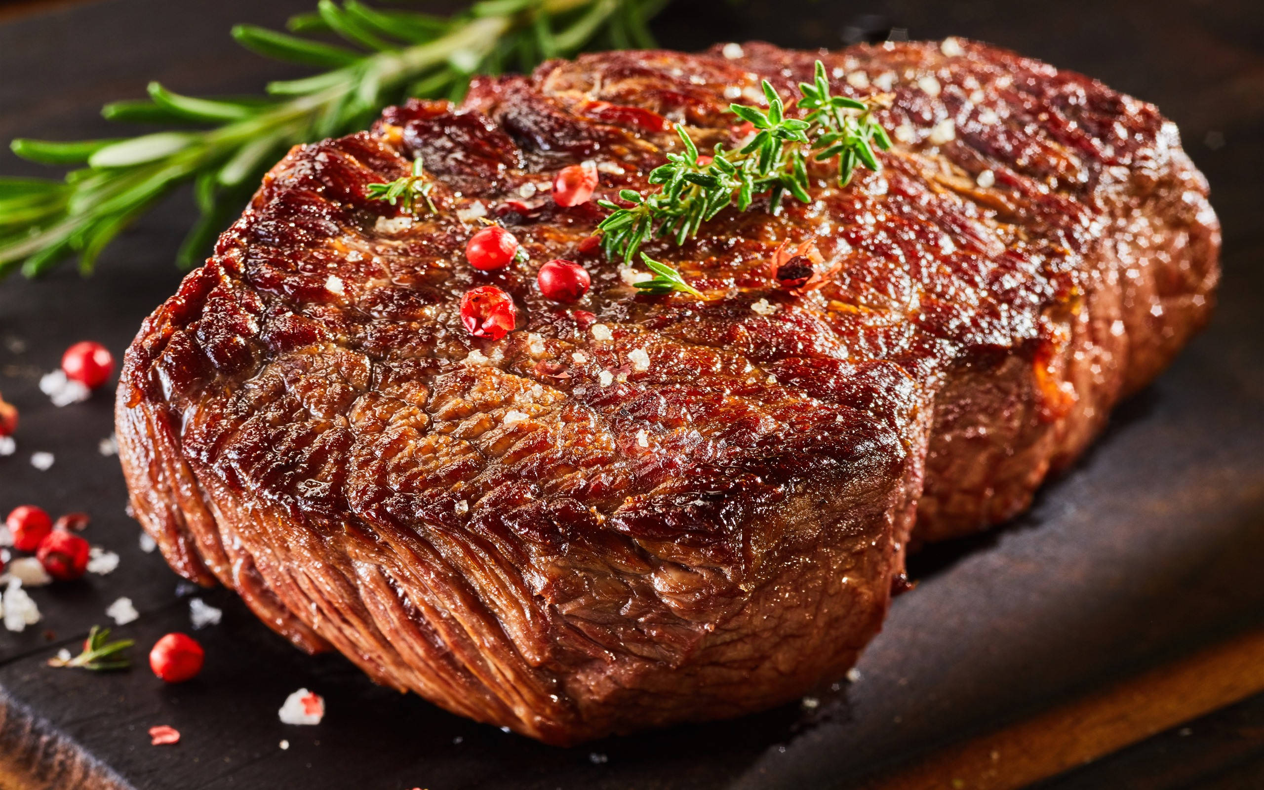 meat 桌布 壁紙 — 完美煎烤的牛排閃爍著鹽和胡椒，配上新鮮迷迭香和紅胡椒粒，放在深色木板上。