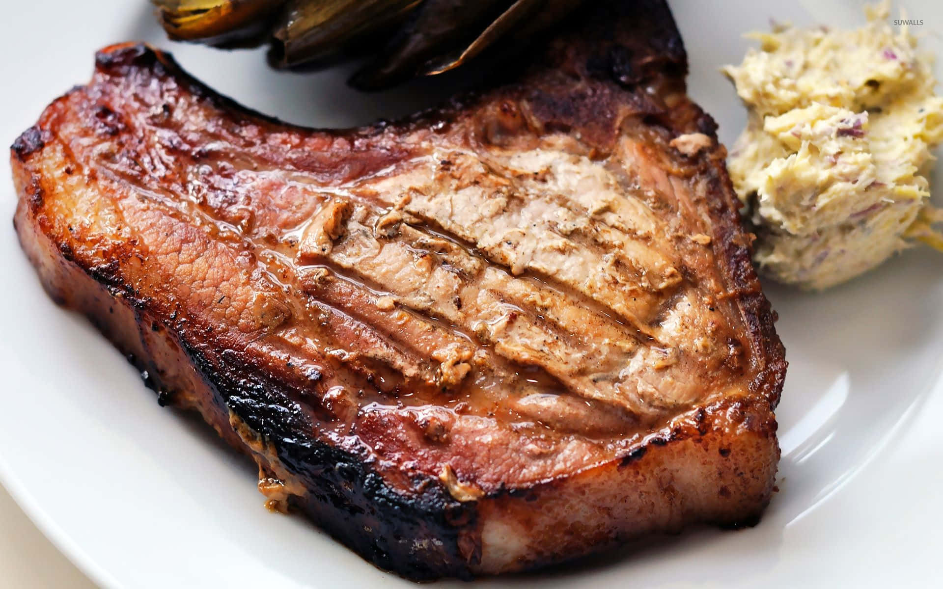 meat 桌布 壁紙 — 完美煎烤的豬排，邊緣酥脆，內部多汁，搭配馬鈴薯泥和烤朝鮮薊，盛放在白色盤子上。