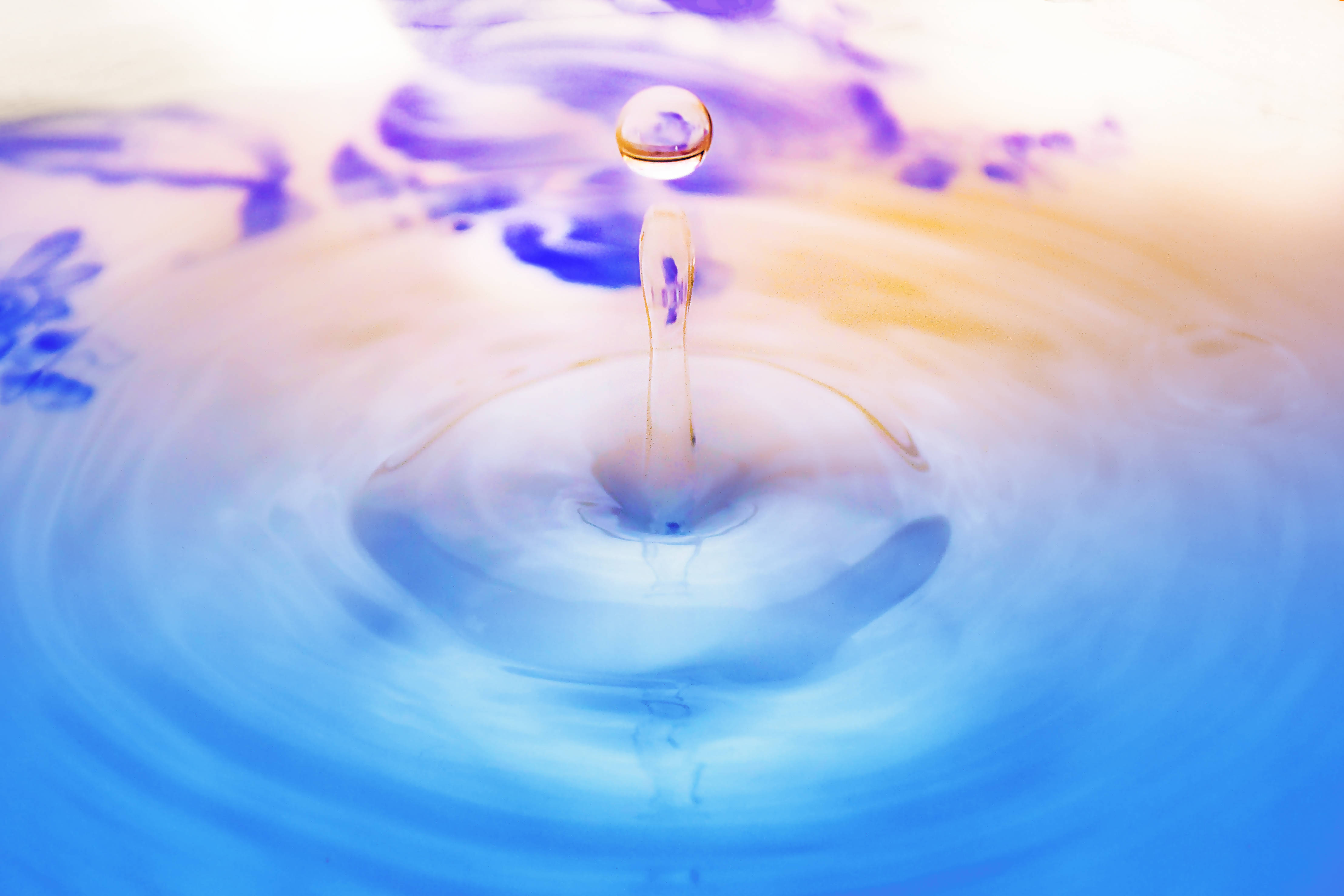 Droplets 桌布 壁紙 — 完美的水滴懸浮在半空中，下方是泛起漣漪的藍色和紫色液體池。