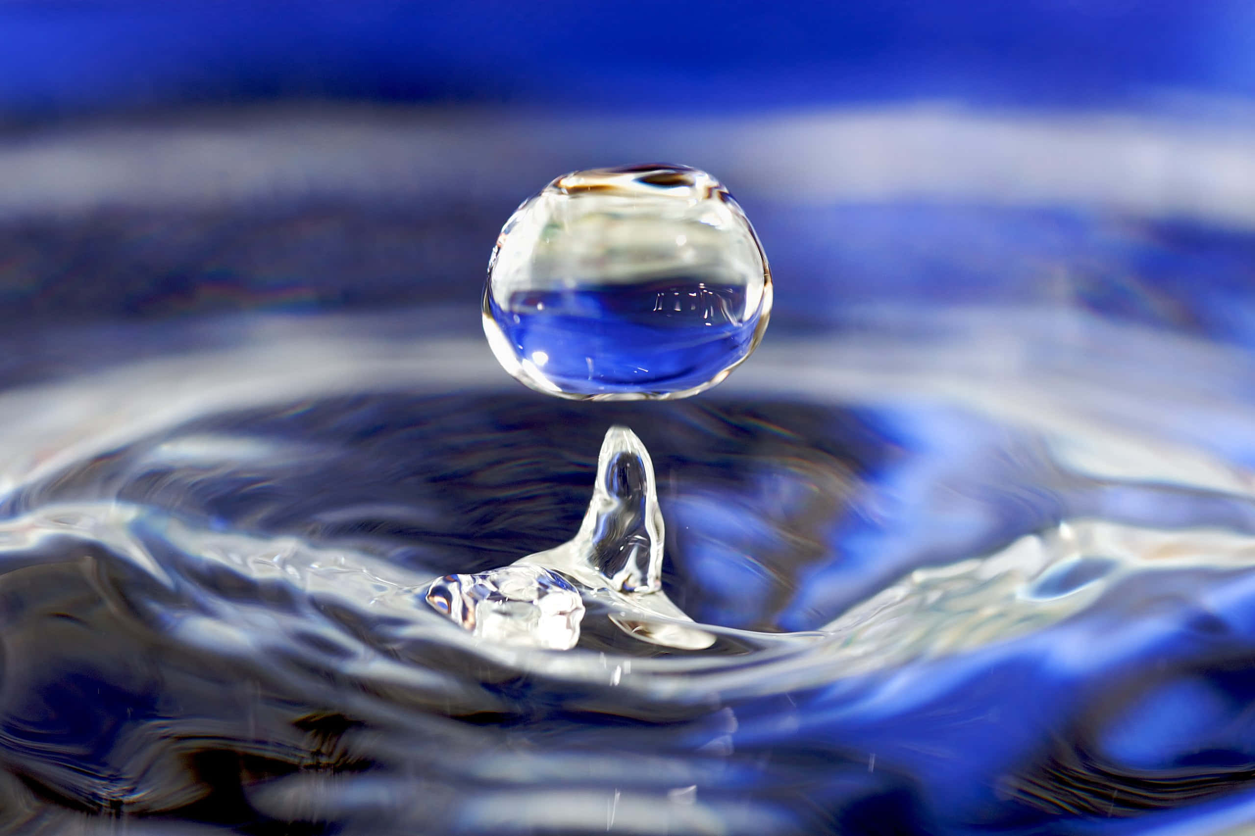 Water Drop 桌布 壁紙 — 完美的水滴懸浮在空中，在漣漪的藍色表面之上，捕捉光線在凍結的運動瞬間。