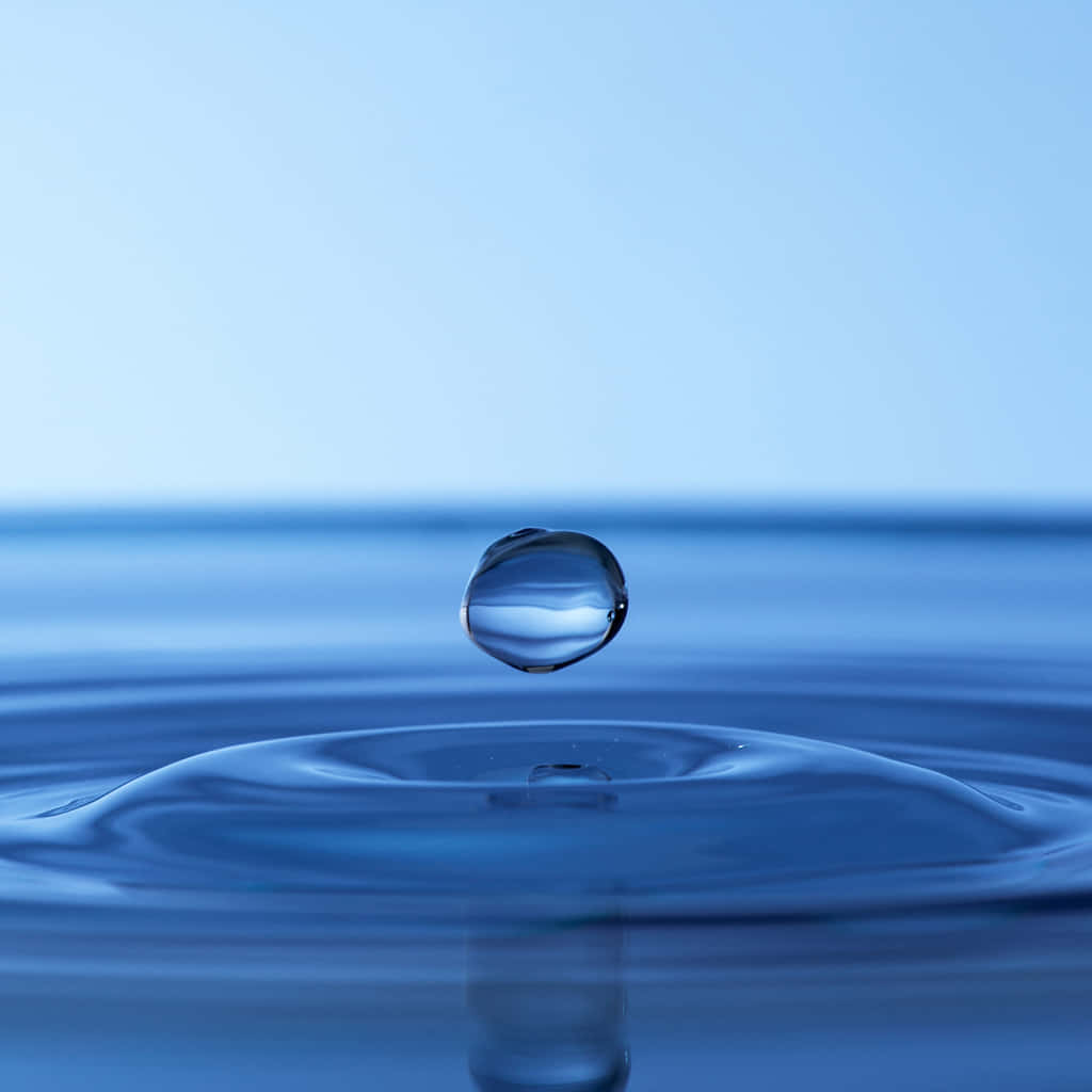 Calming Desktop 桌布 壁紙 — 完美的藍色水滴懸浮在平靜的水面上方，在柔和的日光下形成輕柔的漣漪。
