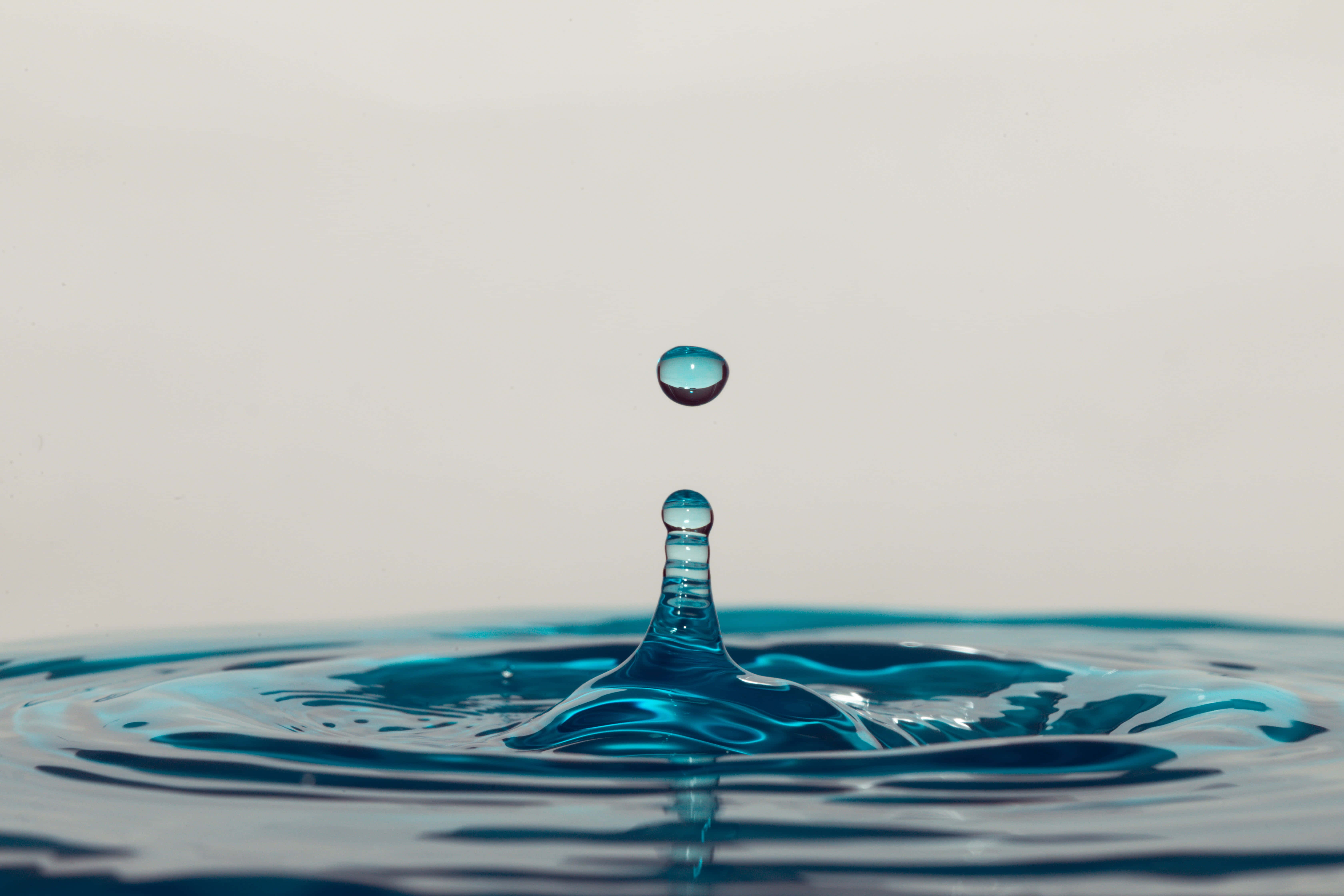 Liquid 桌布 壁紙 — 完美藍色水滴懸浮在半空中，下方是漣漪池面，在極簡風格工作室拍攝中捕捉光線。