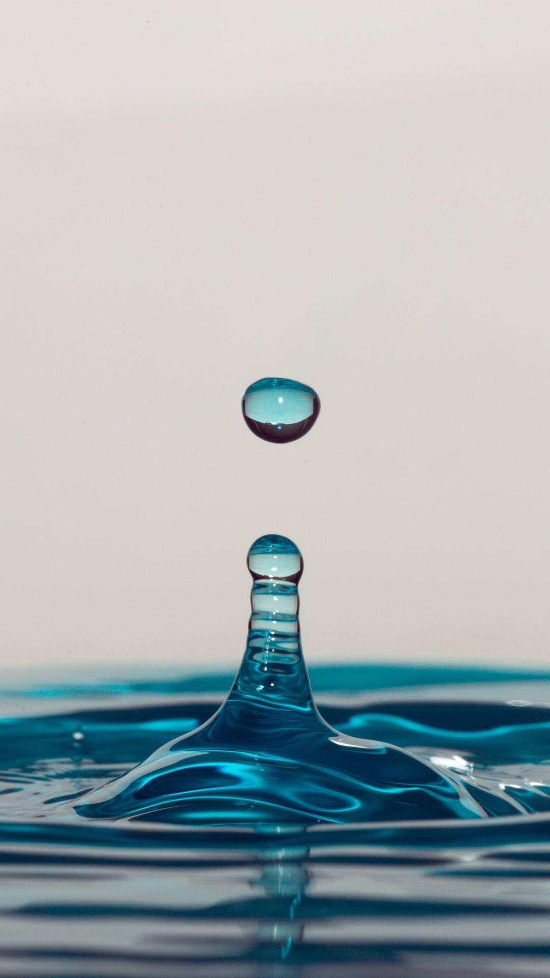 Liquid 桌布 壁紙 — 完美藍色水滴懸浮在半空中，下方是泛起漣漪的水花，背景是柔和的灰色。