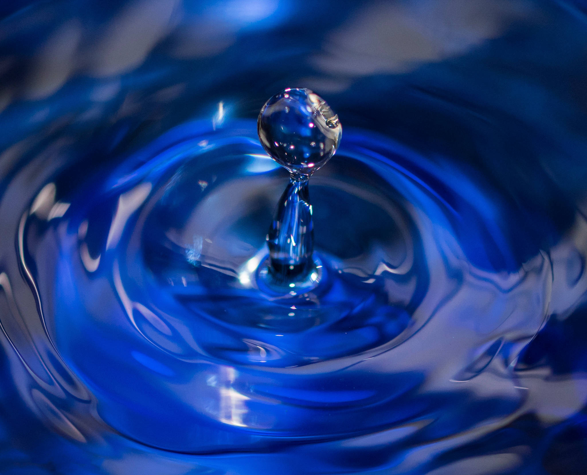 Water Drop 桌布 壁紙 — 完美藍色水滴懸浮在半空中，下方深藍色液體泛起同心漣漪。
