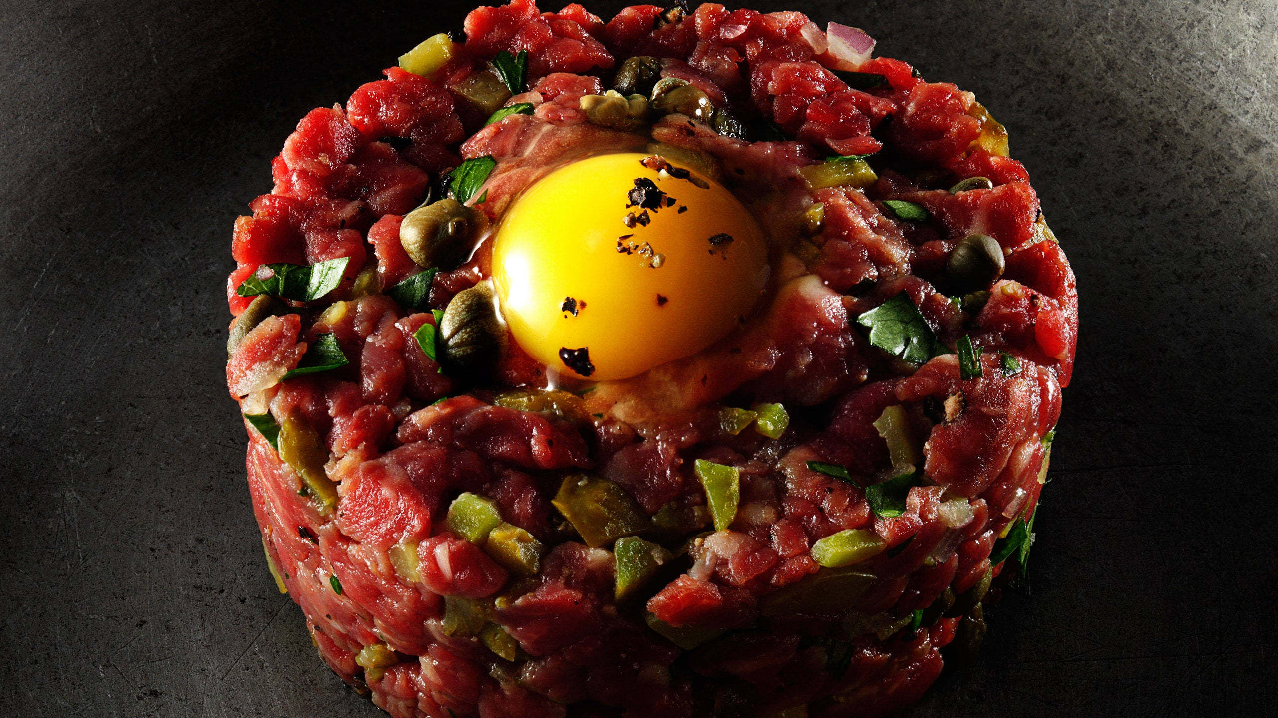 meat 桌布 壁紙 — 完美製作的牛肉他他環，上面放有生蛋黃，並以酸豆和香草點綴，置於深色表面上。