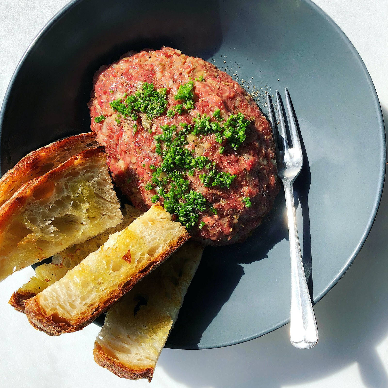 meat 桌布 壁紙 — 完美造型的生牛肉他他，上面鋪滿新鮮細香蔥，旁邊放著烤麵包，置於時尚灰色盤子上，在明亮陽光下呈現。