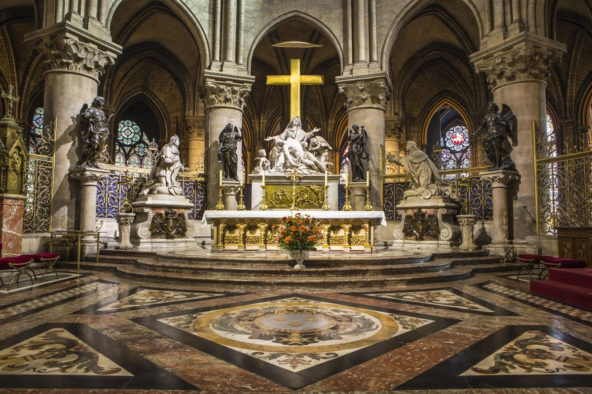 Notre Dame 桌布 壁紙 — 宏偉大教堂內部，金色十字架、大理石地板和彩色玻璃窗沐浴在柔和光線中。