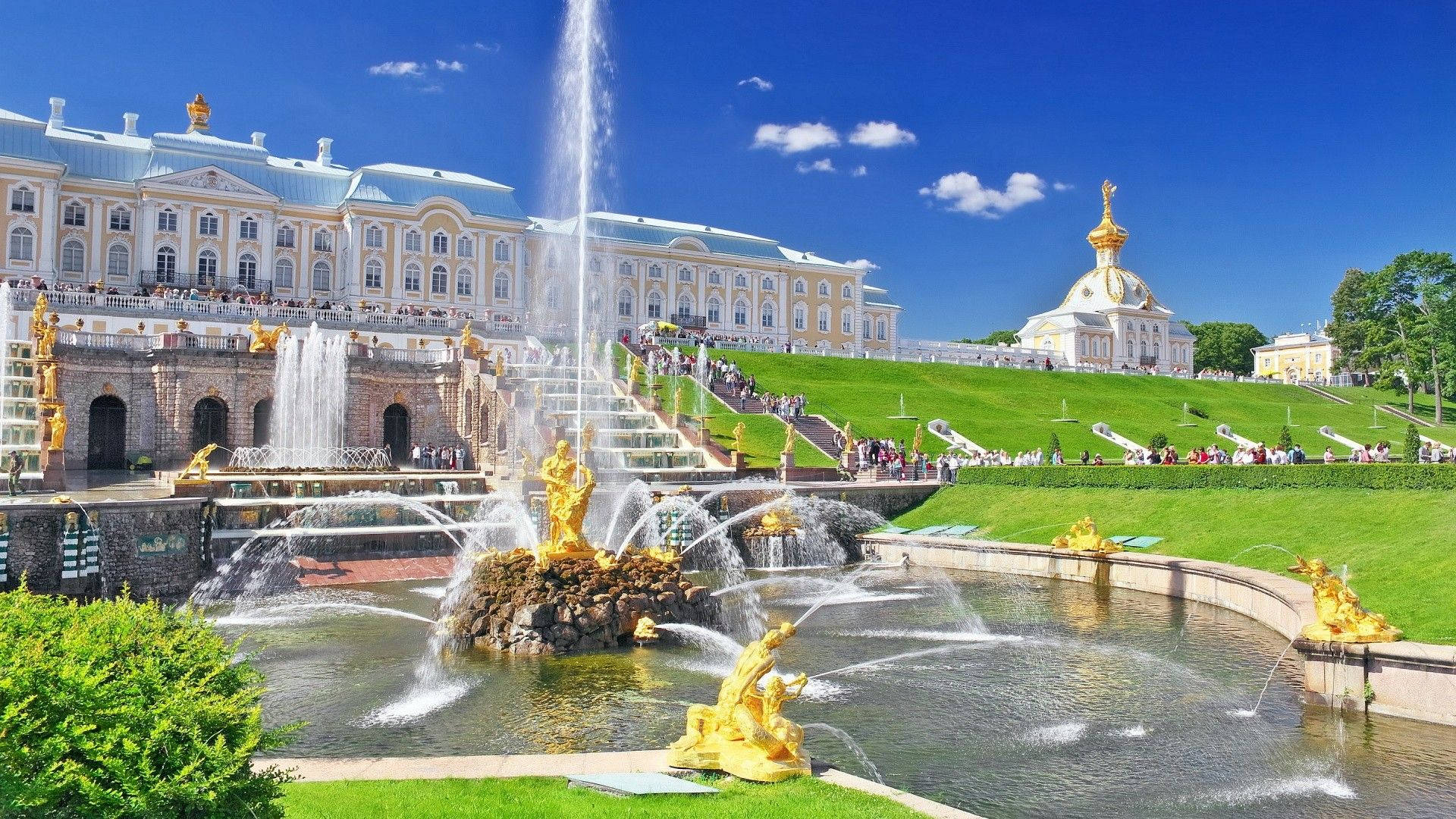 Saint Petersburg 桌布 壁紙 — 宏偉宮殿，金色噴泉在明亮藍天和白雲下噴水。