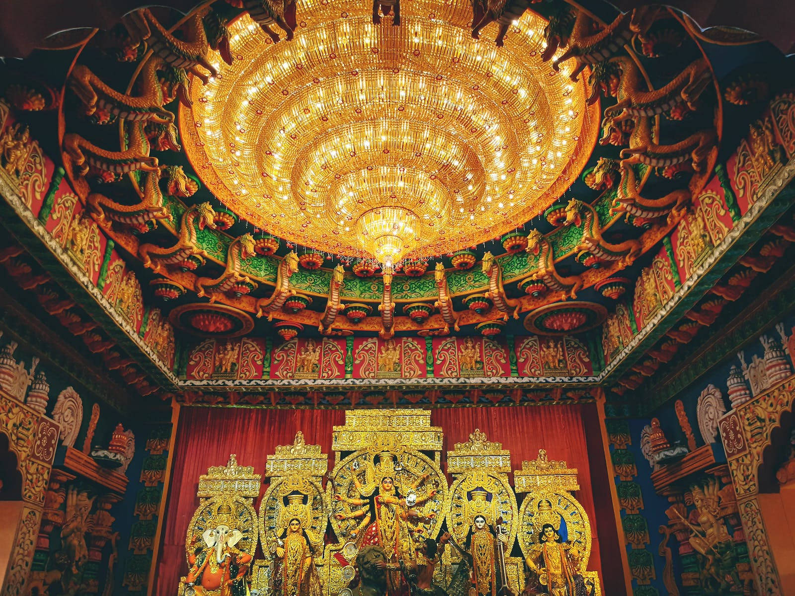 maa durga 桌布 壁紙 — 宏偉寺廟內部，金色神像位於華麗吊燈和彩色雕刻天花板之下。