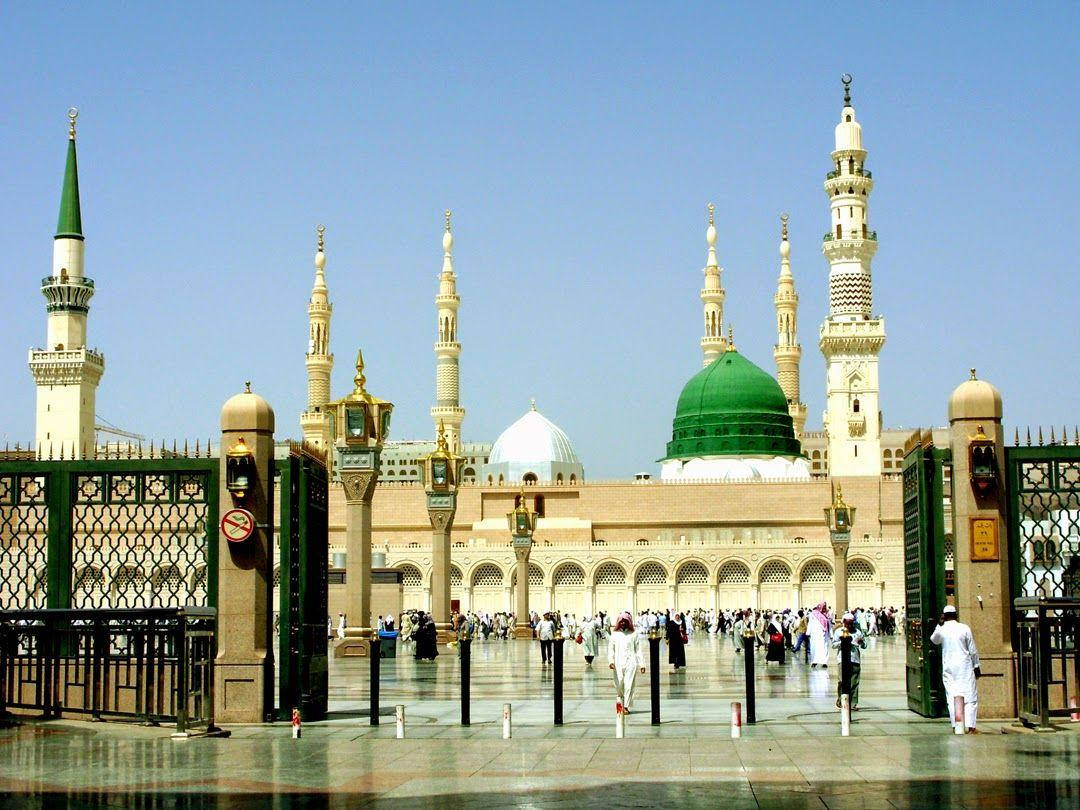 Madina Full HD 桌布 壁紙 — 宏偉清真寺，綠色圓頂和宣禮塔，藍天白雲，庭院中有遊客。