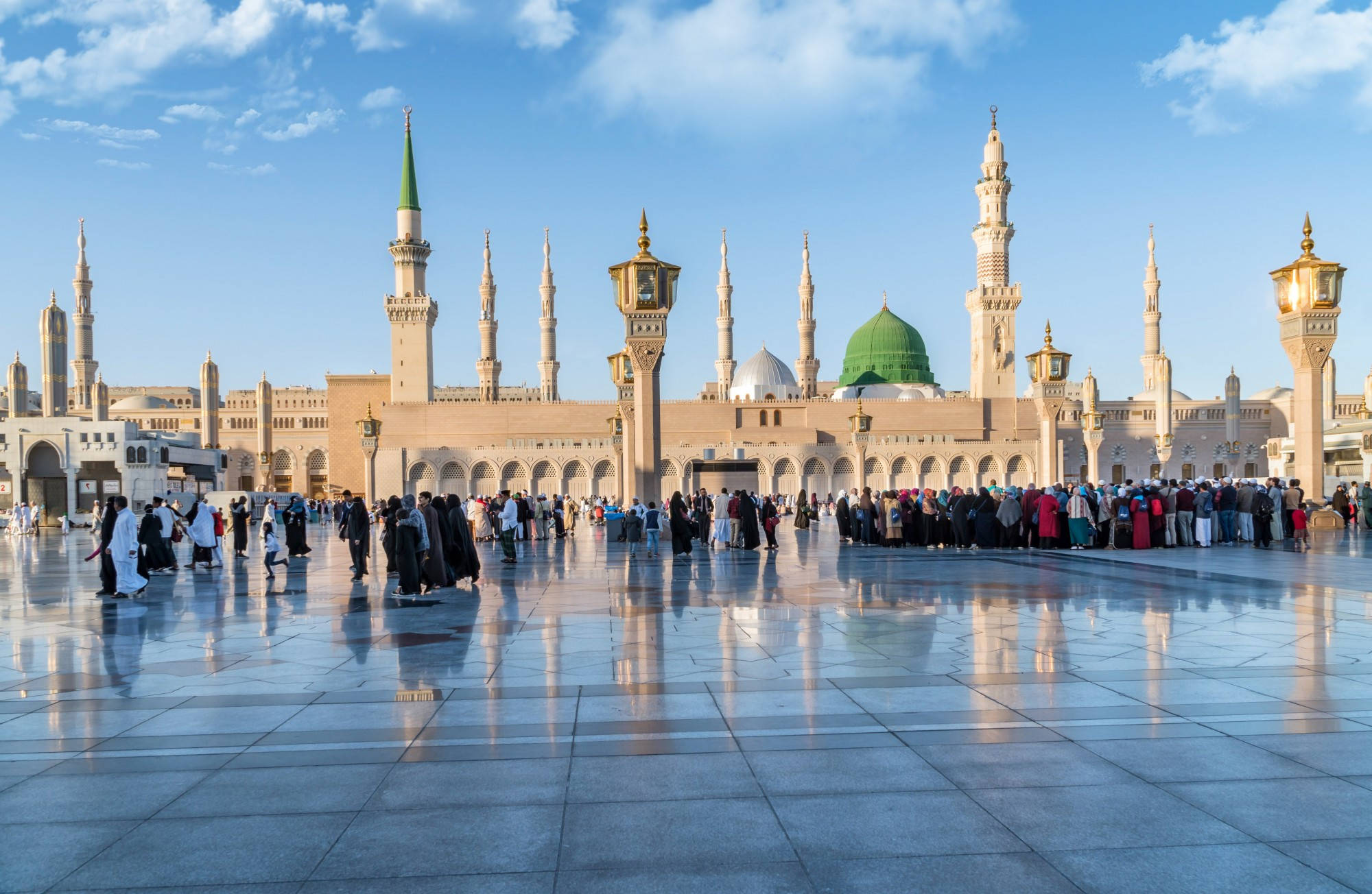 Saudi 桌布 壁紙 — 宏偉清真寺，綠色圓頂和宣禮塔倒映在濕潤的大理石廣場上，天空湛藍。