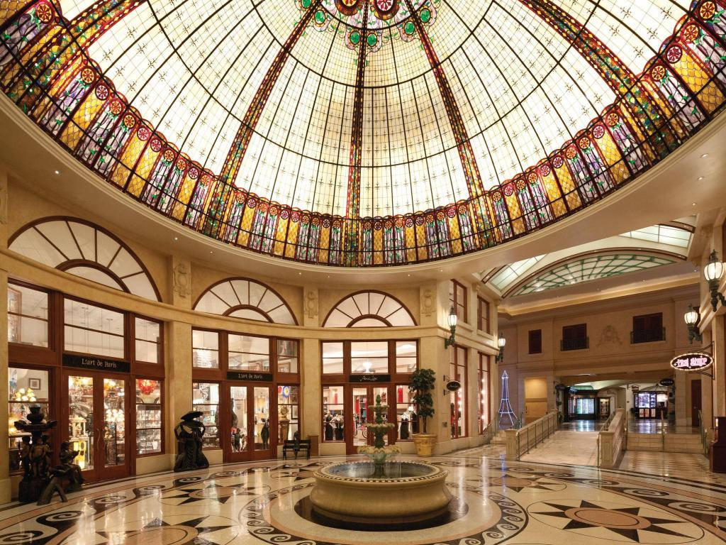 Casino 桌布 壁紙 — 宏偉的中庭，巨大的彩色玻璃圓頂將五彩斑斕的光線投射到大理石地板噴泉和拱形商店門面上。