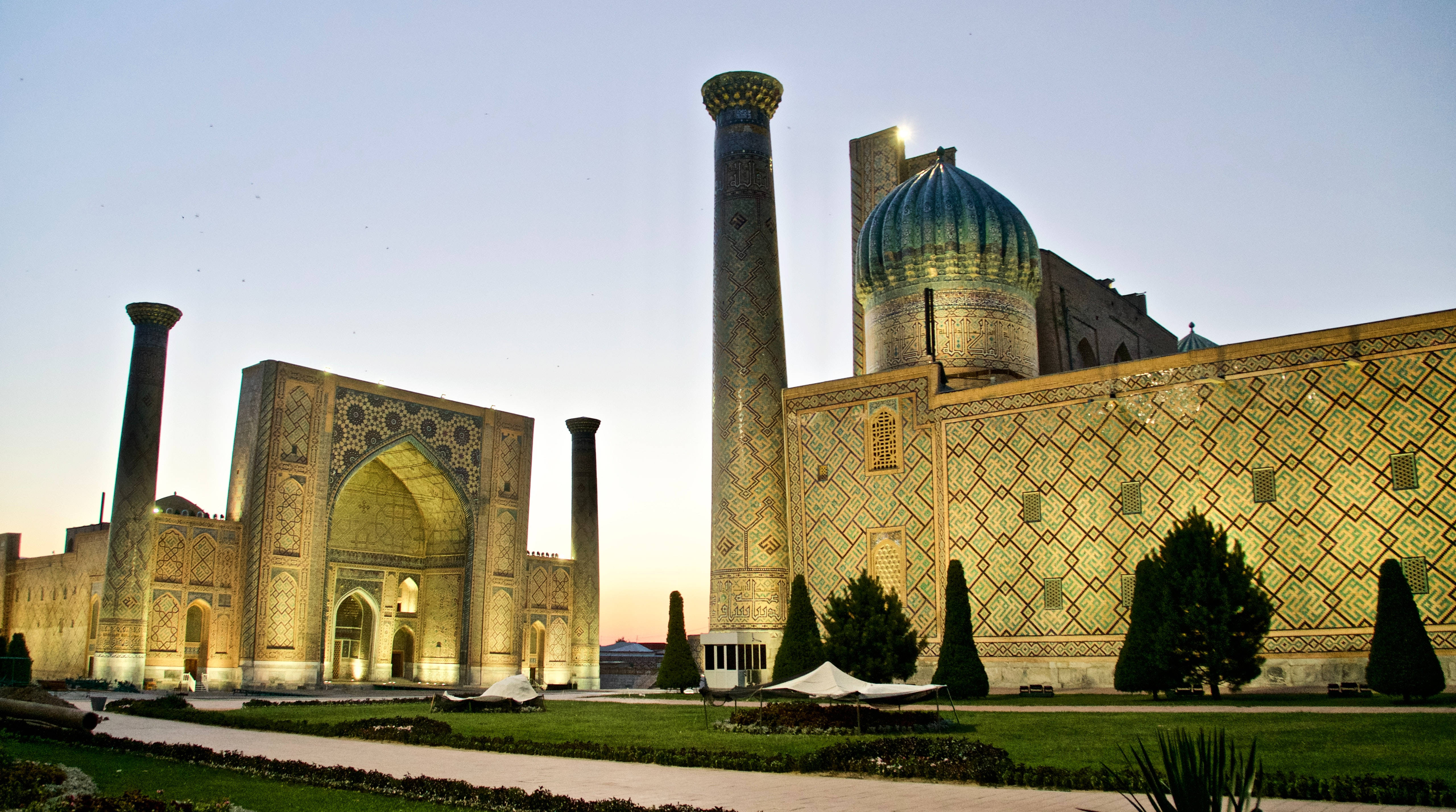 Uzbekistan 桌布 壁紙 — 宏偉的伊斯蘭建築，擁有宣禮塔和藍色圓頂，在黃昏時分柔和天空下被照亮。