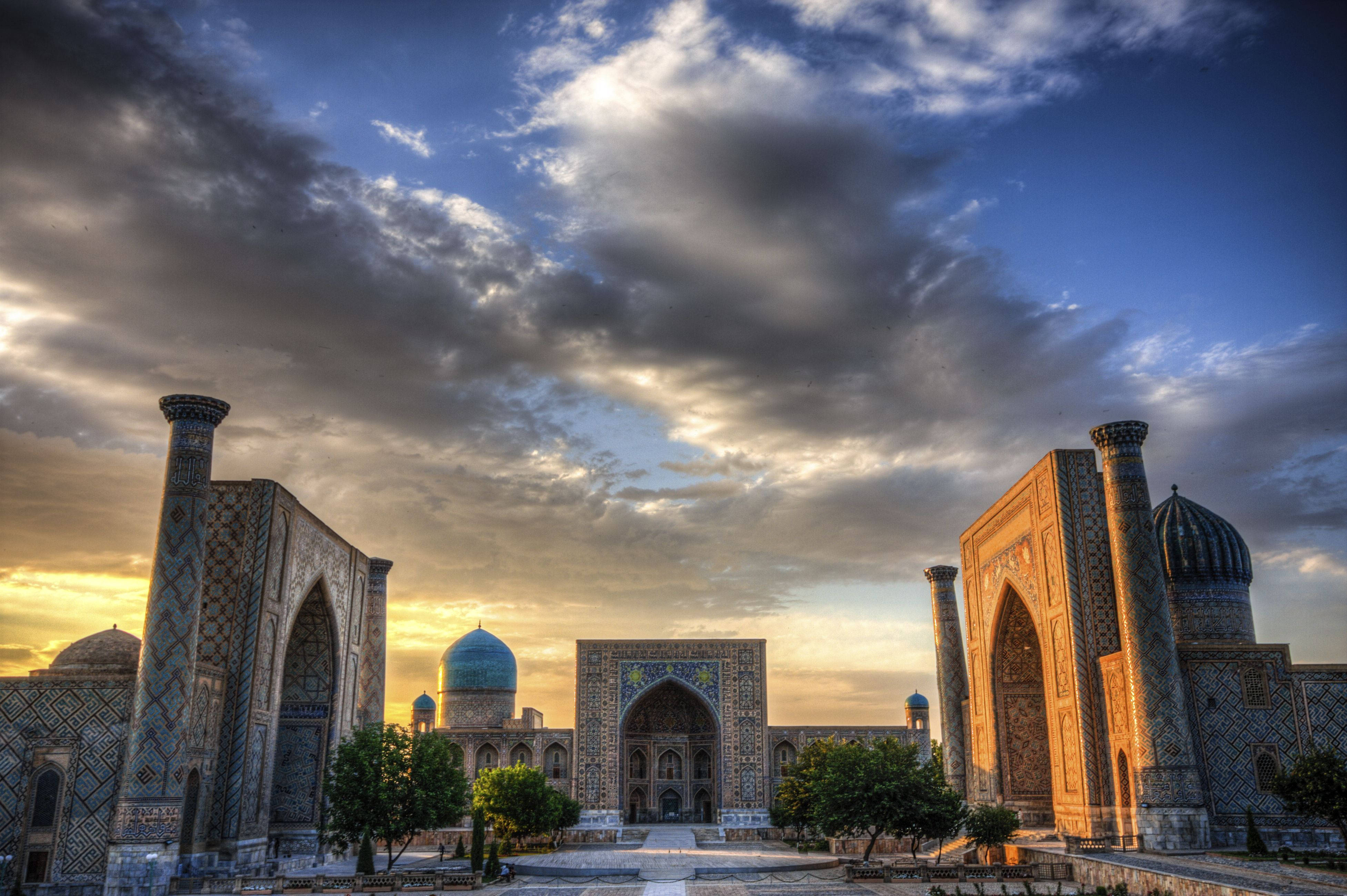 Uzbekistan 桌布 壁紙 — 宏偉的伊斯蘭建築，擁有綠松石色的圓頂和精緻的瓷磚工藝，在戲劇性的雲層下沐浴在金色的日落光芒中。
