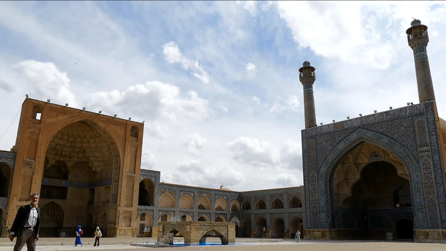 Iran 桌布 壁紙 — 宏偉的伊斯蘭清真寺庭院，高聳的宣禮塔和精緻的藍色瓷磚工藝，天空部分多雲。