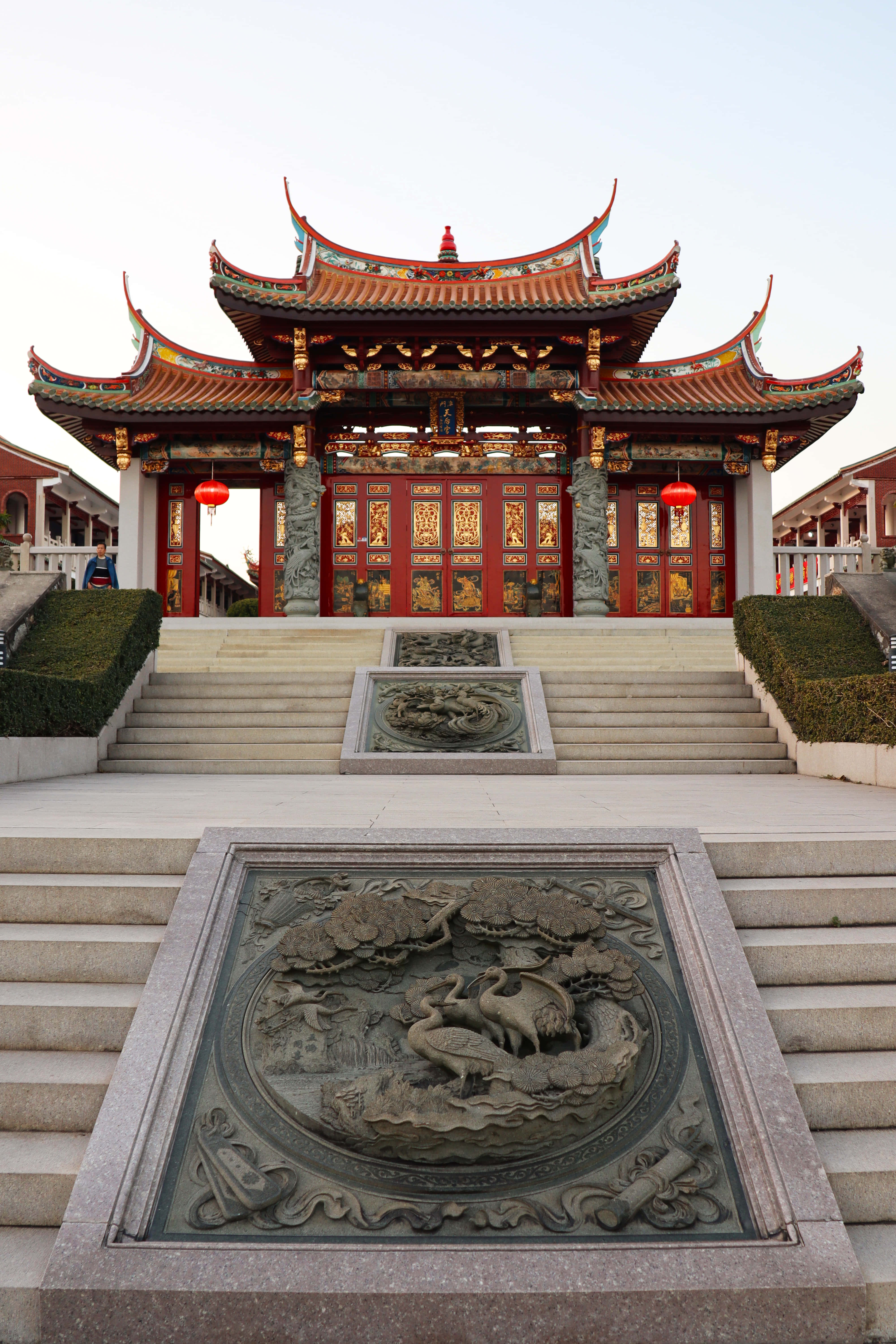 中文 桌布 壁紙 — 宏偉的傳統中國寺廟，紅頂和華麗雕刻，矗立在石階之上，兩旁是綠色樹籬。