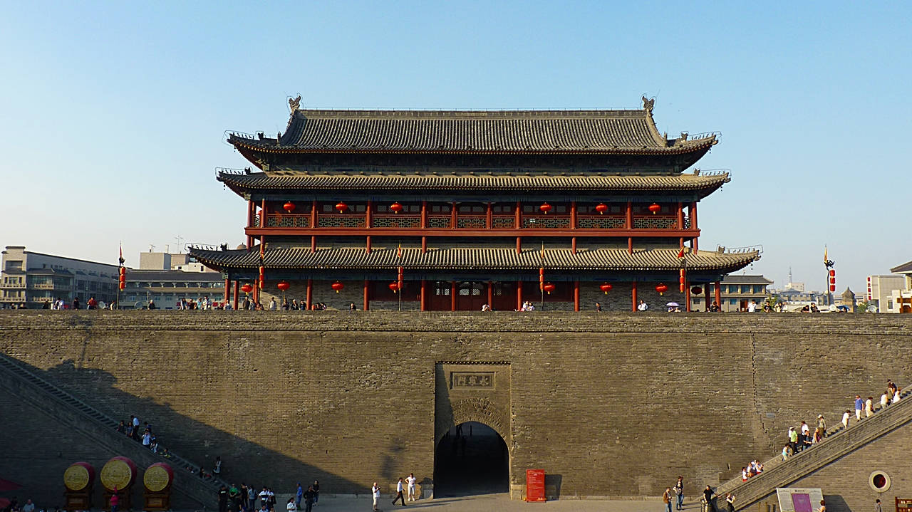 Xian 桌布 壁紙 — 宏偉的傳統中式門樓，掛著紅燈籠，矗立在古老的石牆上，天空湛藍清澈。
